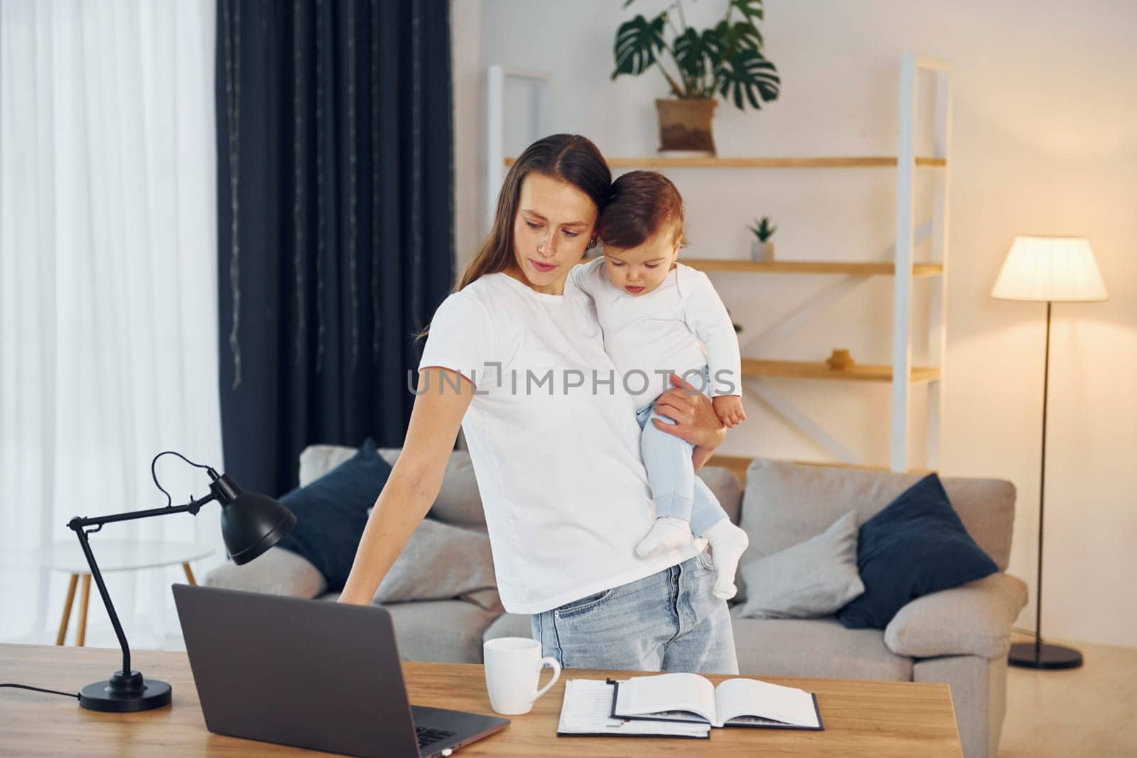 Using laptop. Mother with her little daughter is at home together.