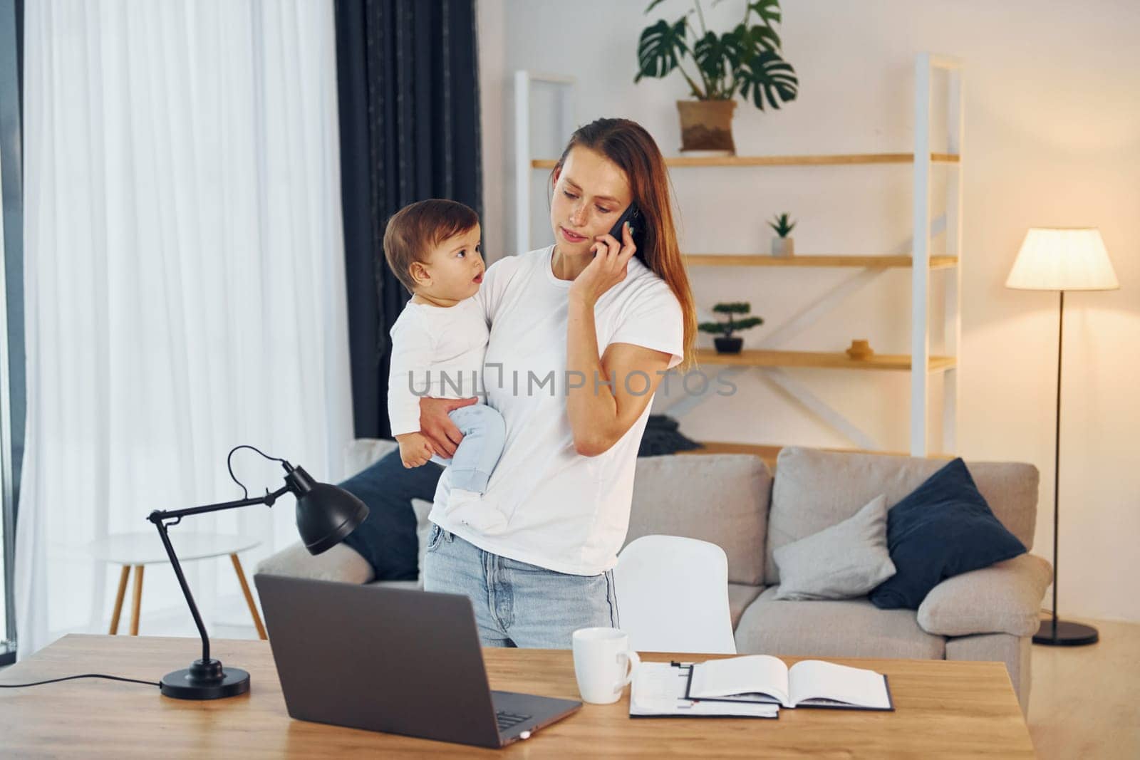 Laptop is on the table. Mother with her little daughter is at home together.