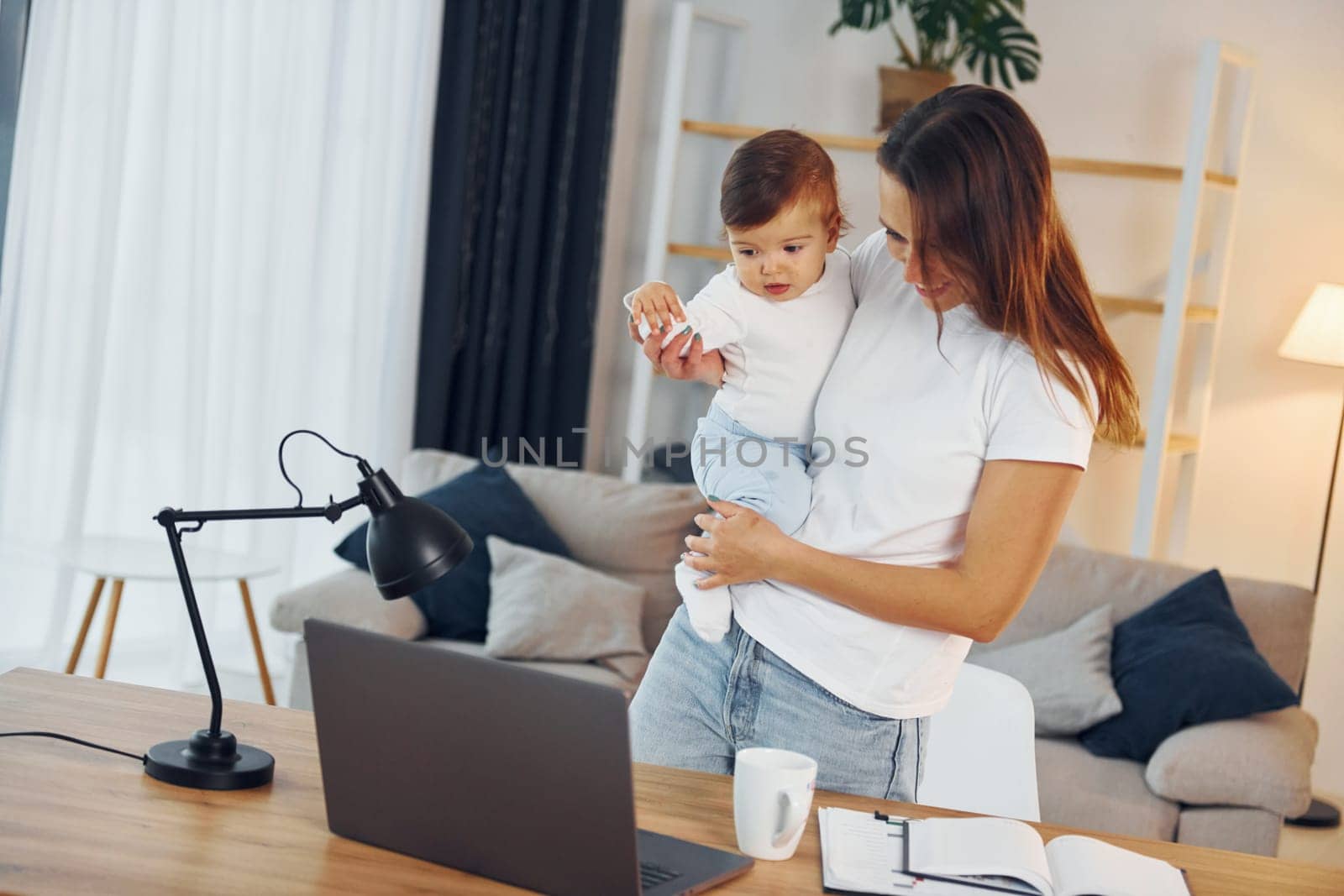 Laptop is on the table. Mother with her little daughter is at home together.