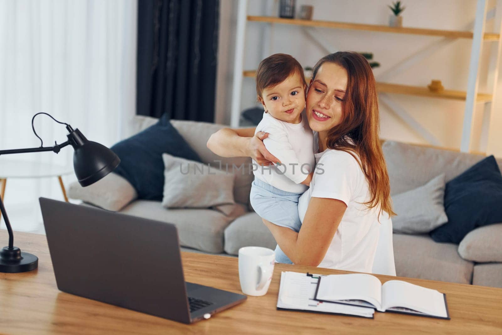Laptop is on the table. Mother with her little daughter is at home together.