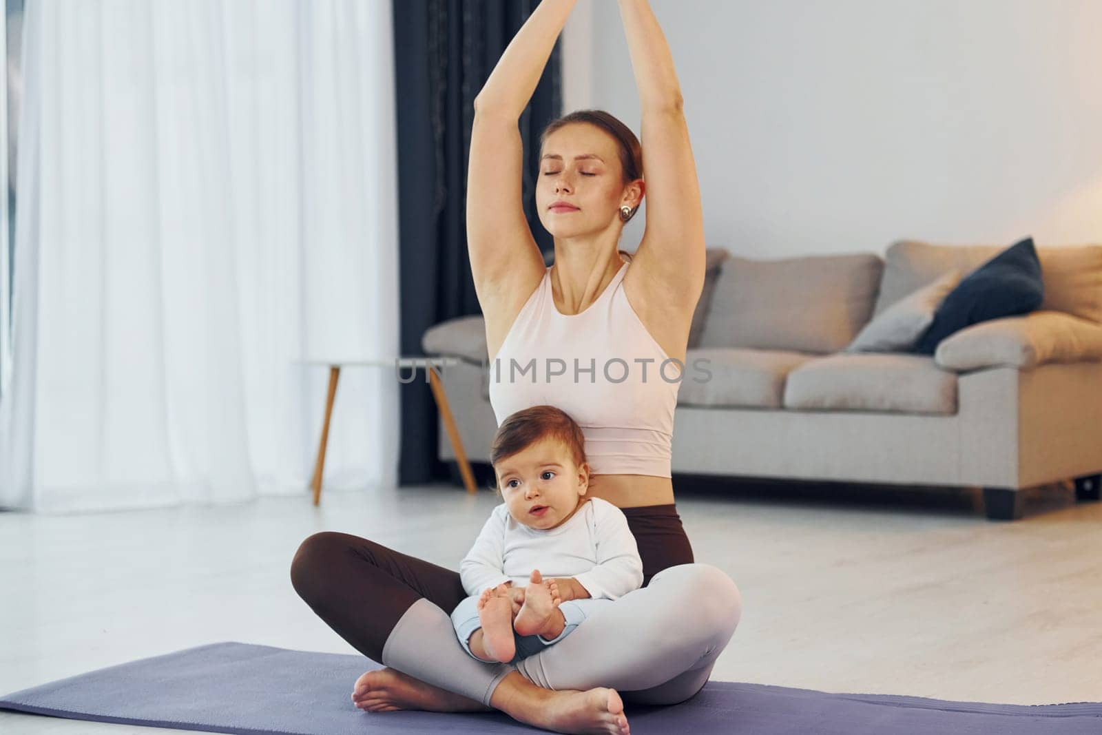 Doing yoga exercises. Mother with her little daughter is at home together by Standret