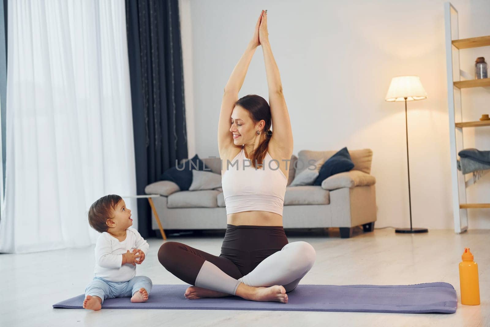 Doing exercises on the mat. Mother with her little daughter is at home together.