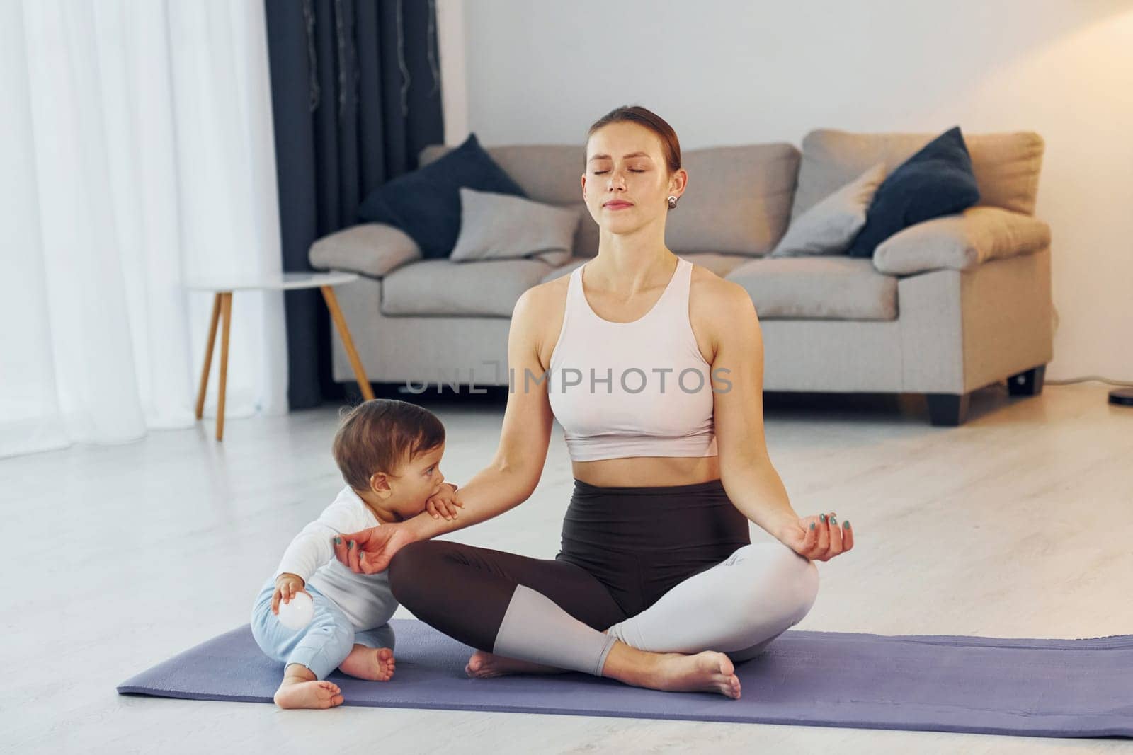 Doing exercises on the mat. Mother with her little daughter is at home together.