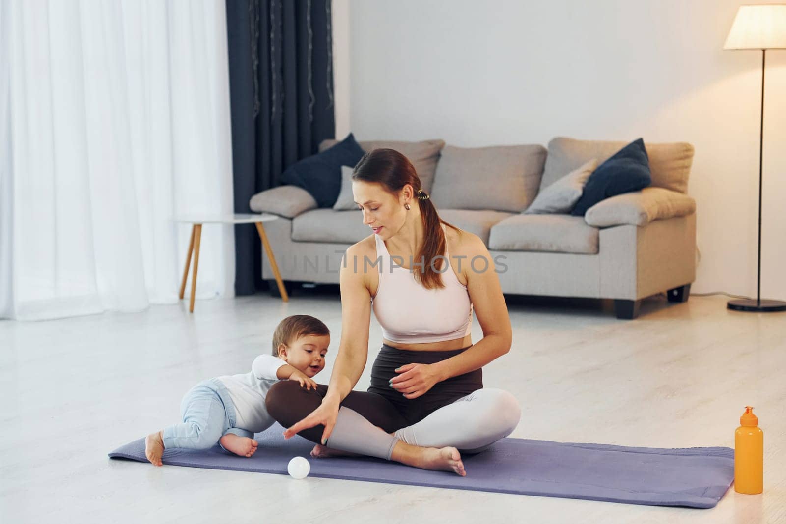 Doing exercises on the mat. Mother with her little daughter is at home together by Standret