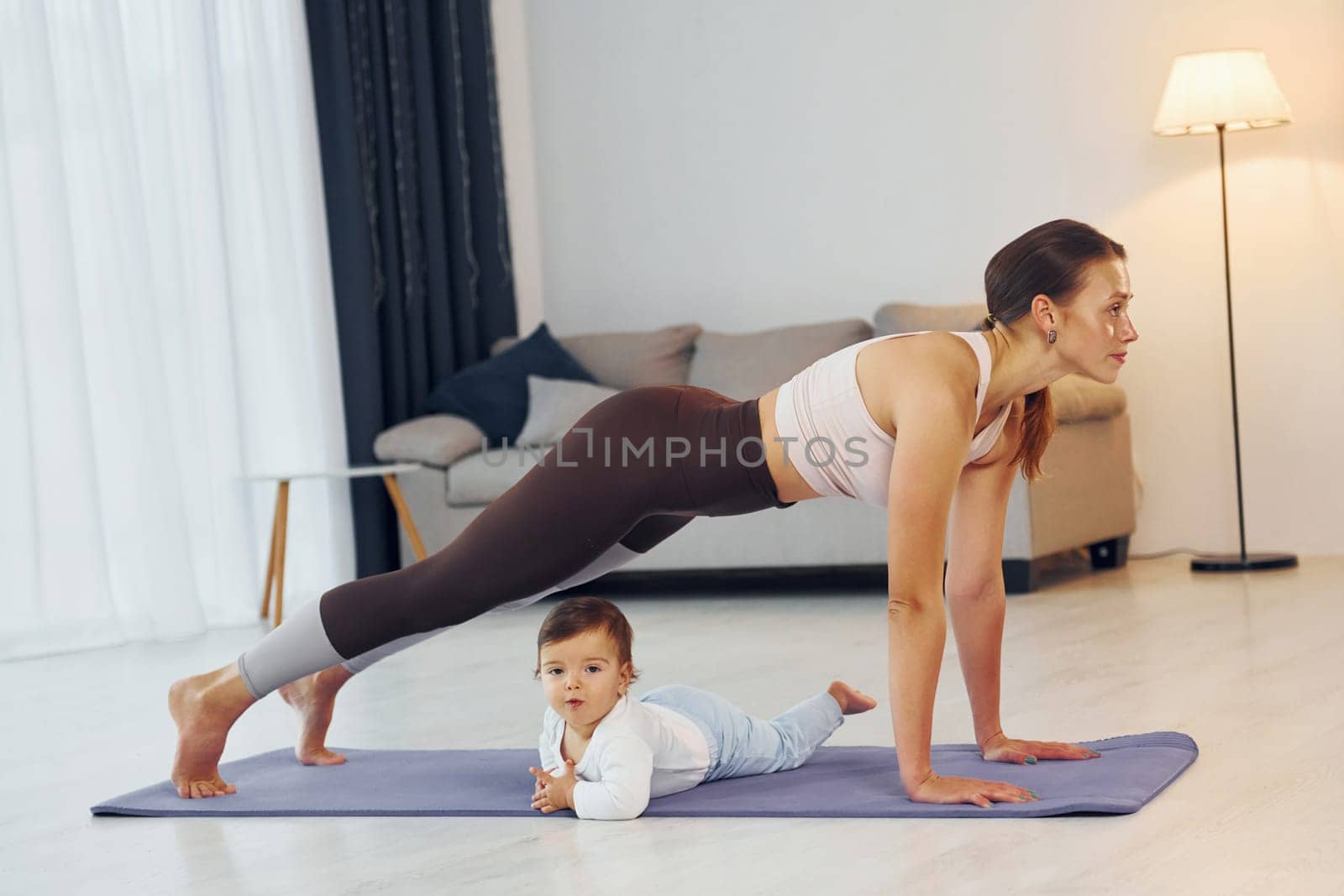 Doing exercises on the mat. Mother with her little daughter is at home together by Standret