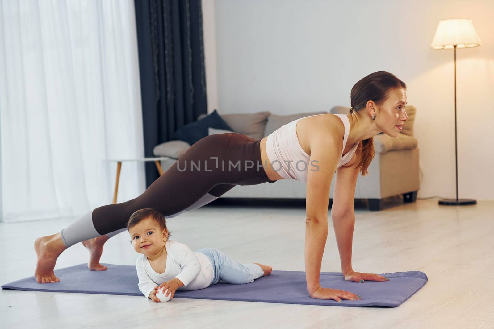 Doing exercises on the mat. Mother with her little daughter is at home together.