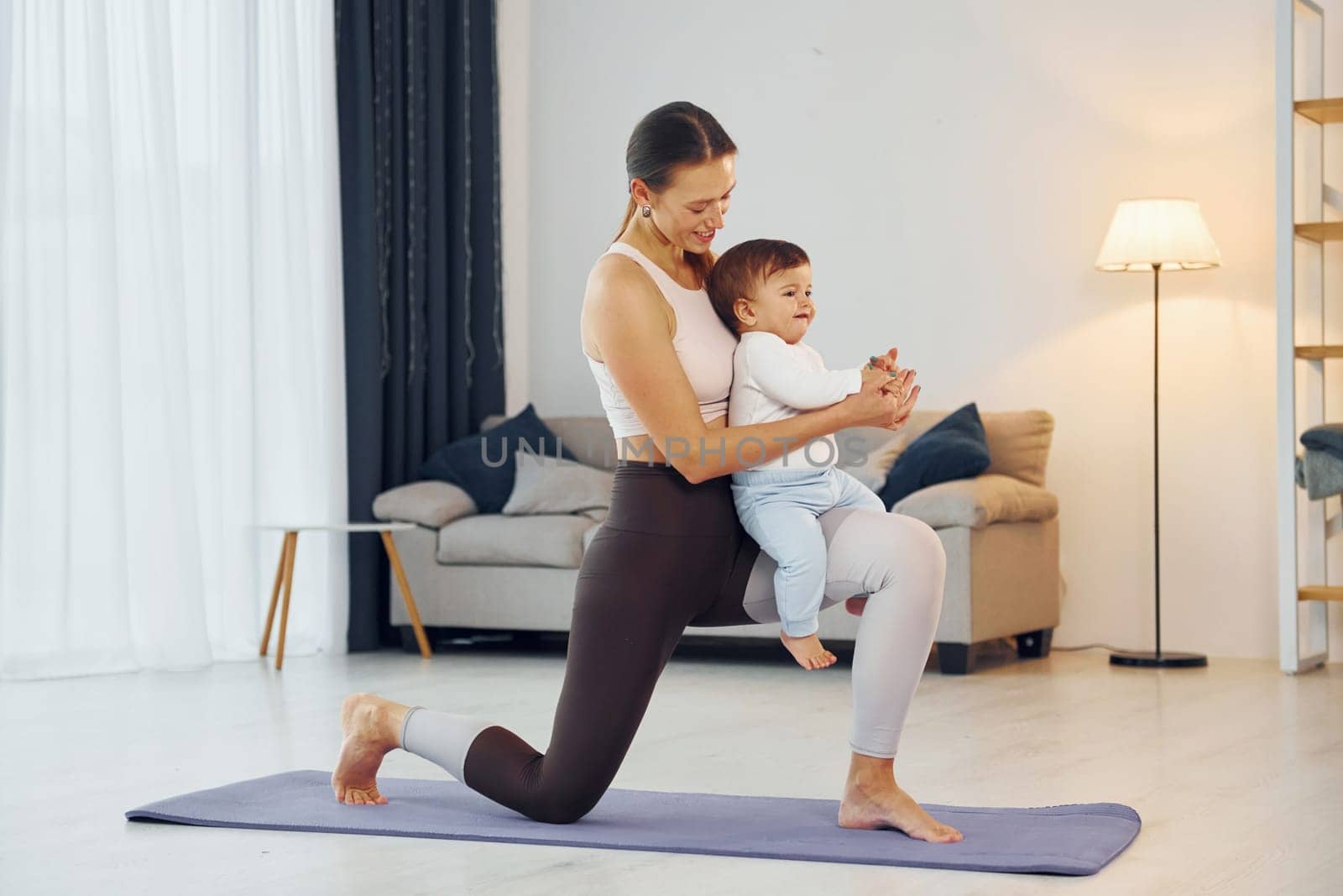 Standing on the mat and doing exerises. Mother with her little daughter is at home together.