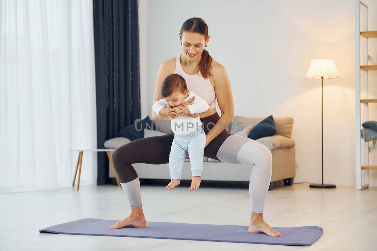 Standing on the mat and doing exerises. Mother with her little daughter is at home together by Standret