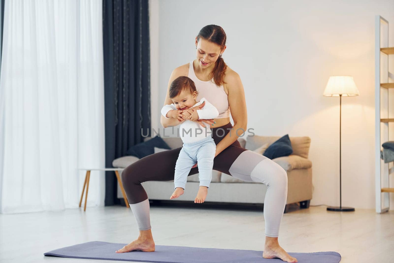 Standing on the mat and doing exerises. Mother with her little daughter is at home together.