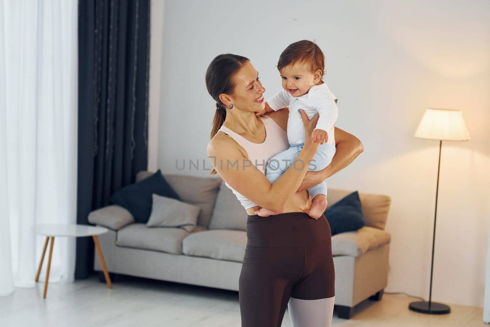 Woman in sportive clothes holding little girl. Mother with her little daughter is at home together.