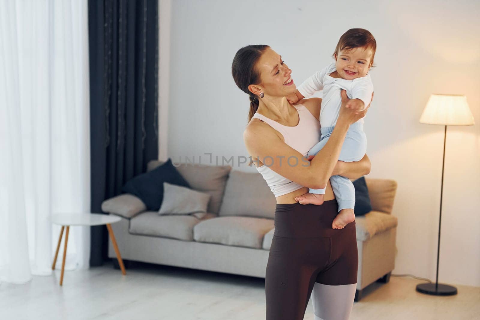 Woman in sportive clothes holding little girl. Mother with her little daughter is at home together.