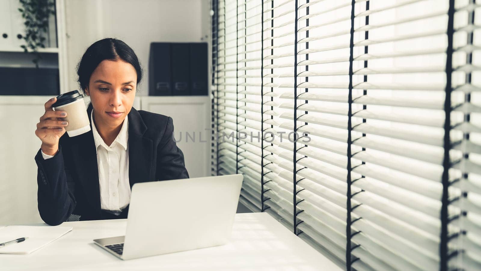 Competent female employee sits at her desk with a cup of coffee. Modern employee working with a drink, recreation during working hours, caffeine for people who are working