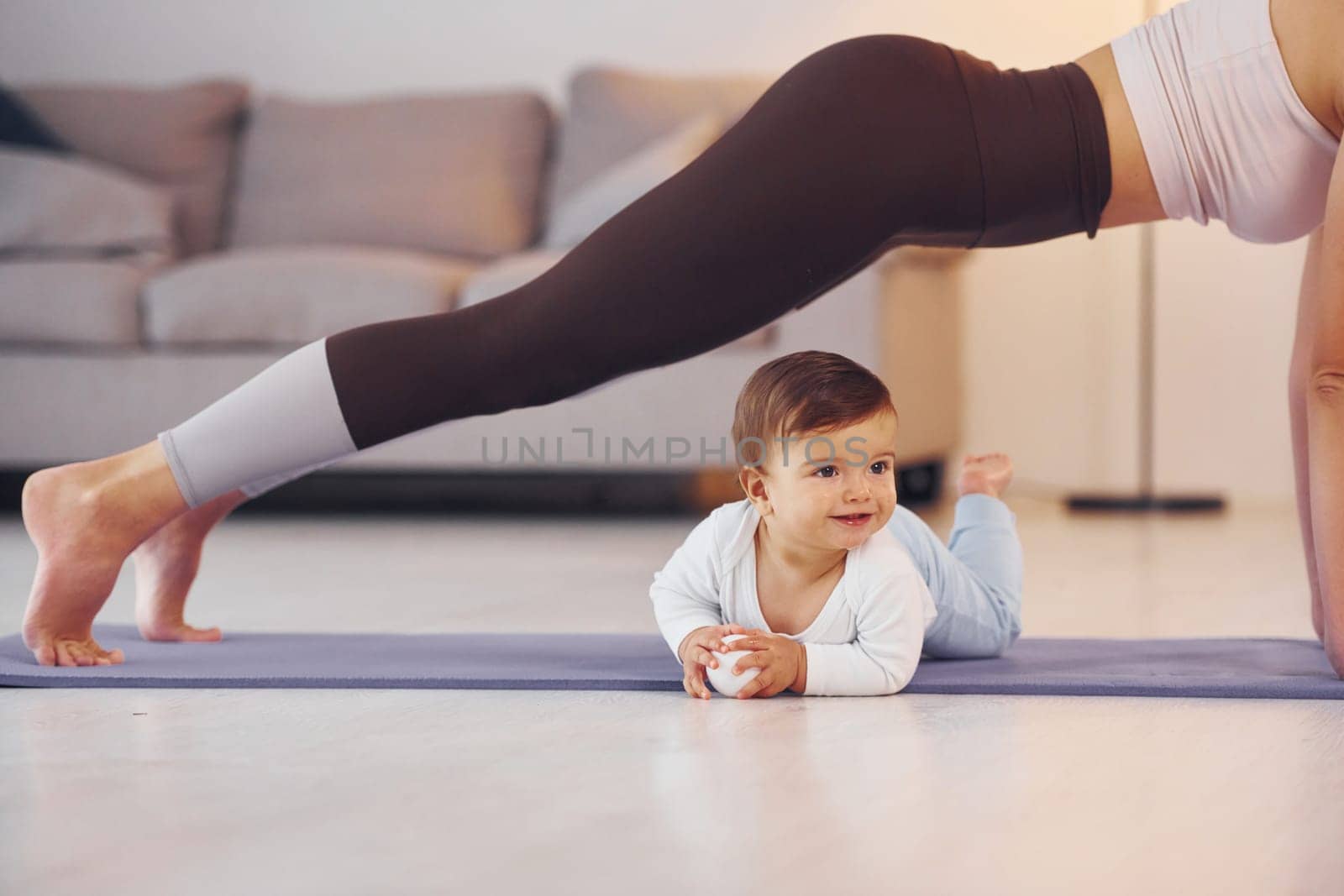 Woman doing exercises. Mother with her little daughter is at home together.