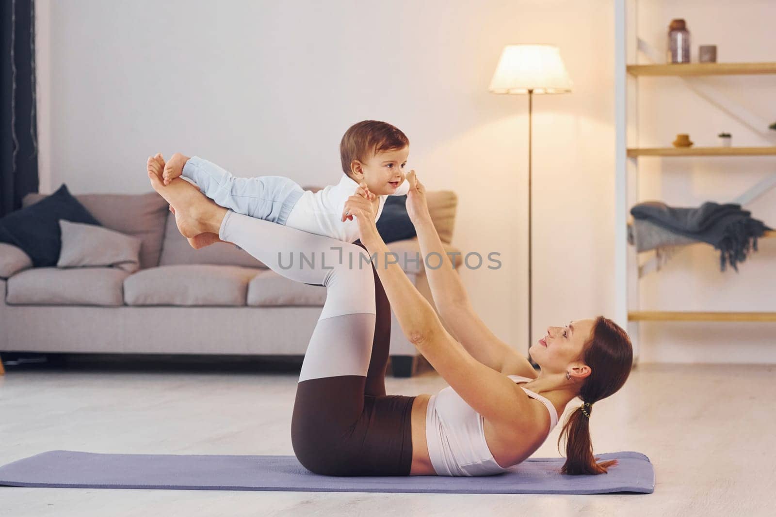 Side view of woman that doing exercises with little girl. Mother with her little daughter is at home together.