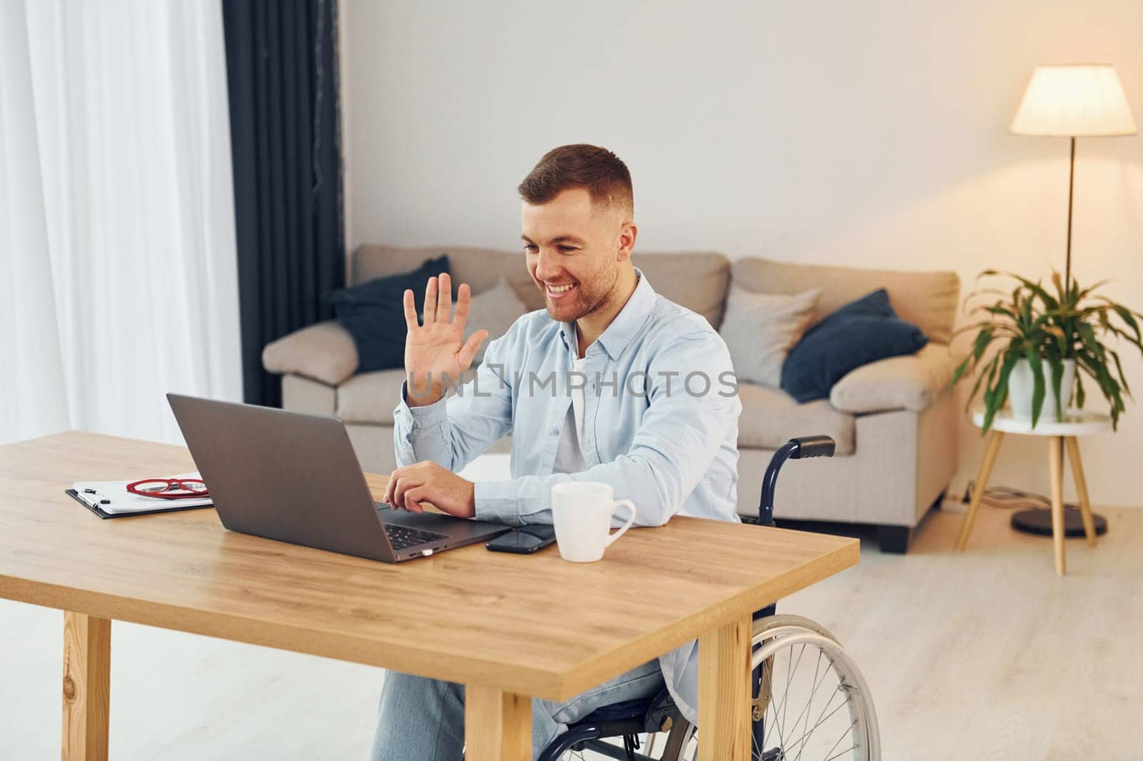 Laptop on the table. Disabled man in wheelchair is at home.