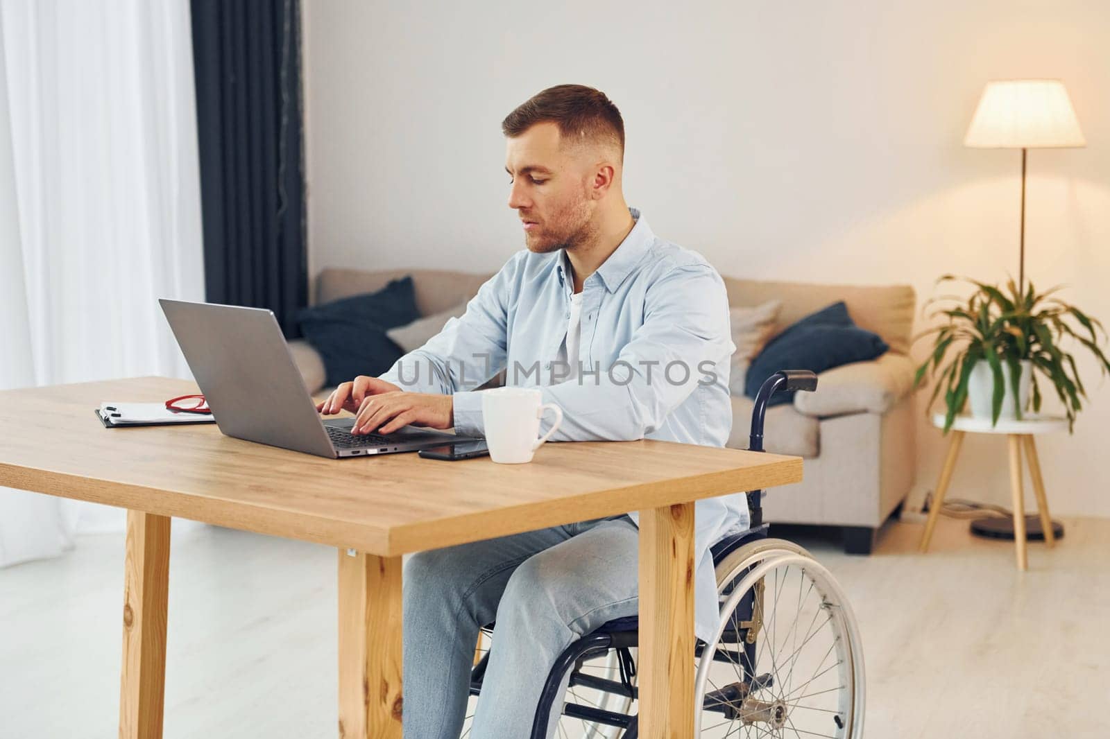 Laptop on the table. Disabled man in wheelchair is at home.