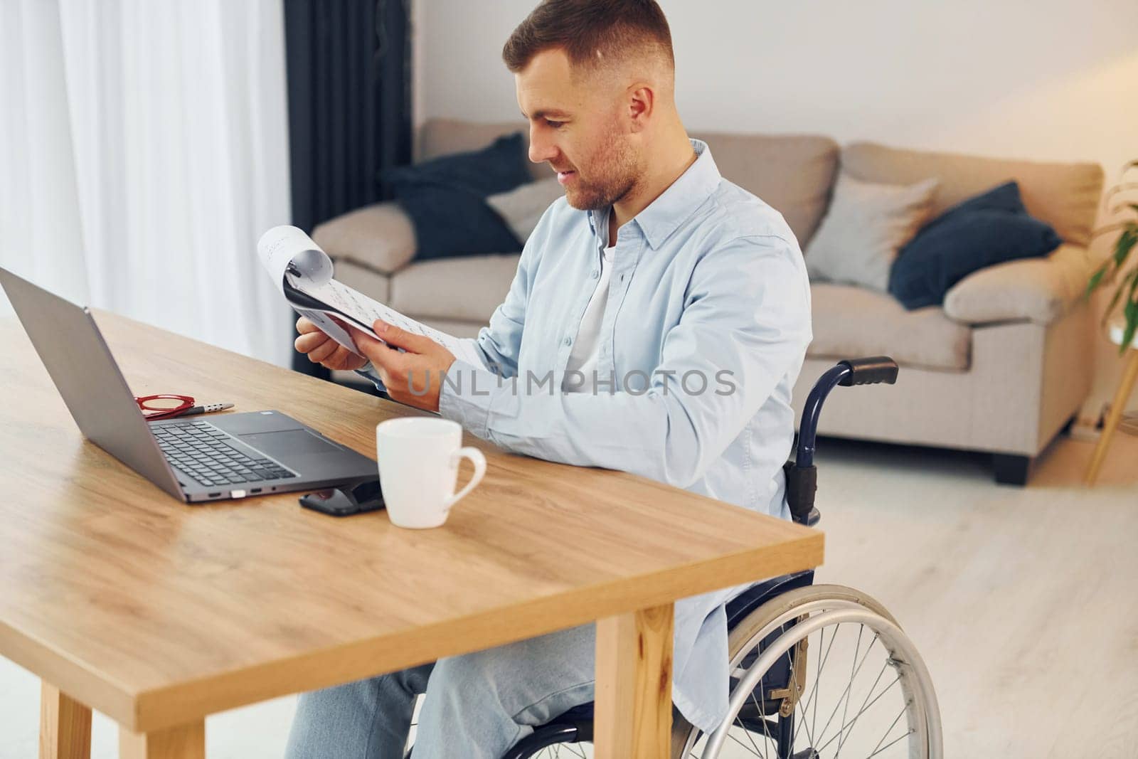 Laptop on the table. Disabled man in wheelchair is at home.