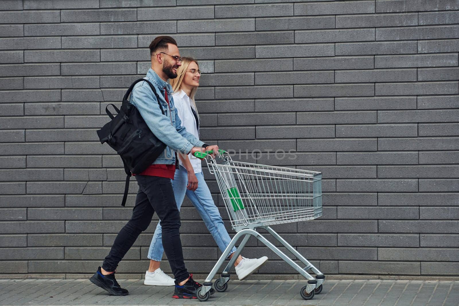 With shopping cart. Young stylish man with woman in casual clothes outdoors together. Conception of friendship or relationships.