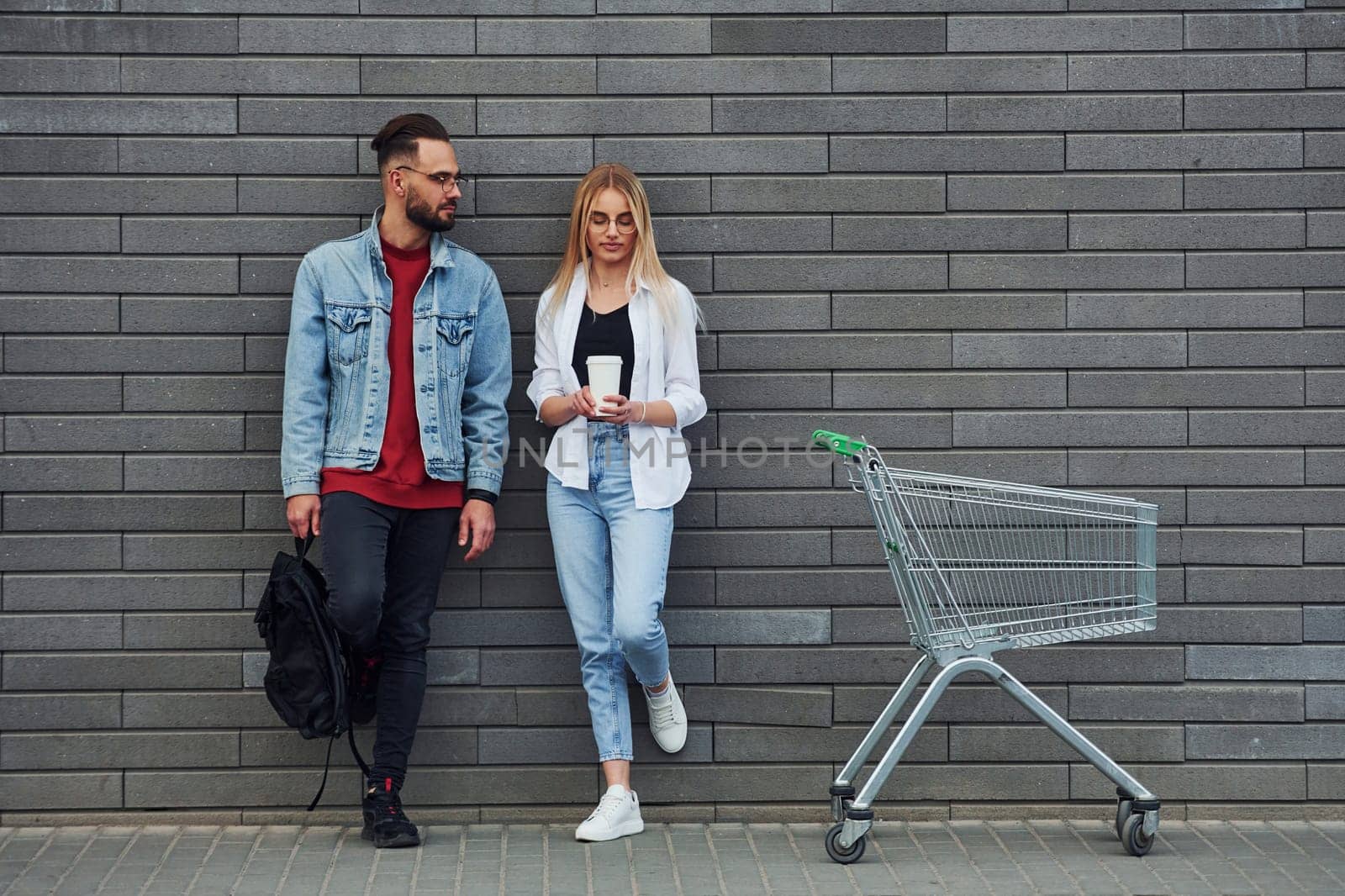 With shopping cart. Young stylish man with woman in casual clothes outdoors together. Conception of friendship or relationships.