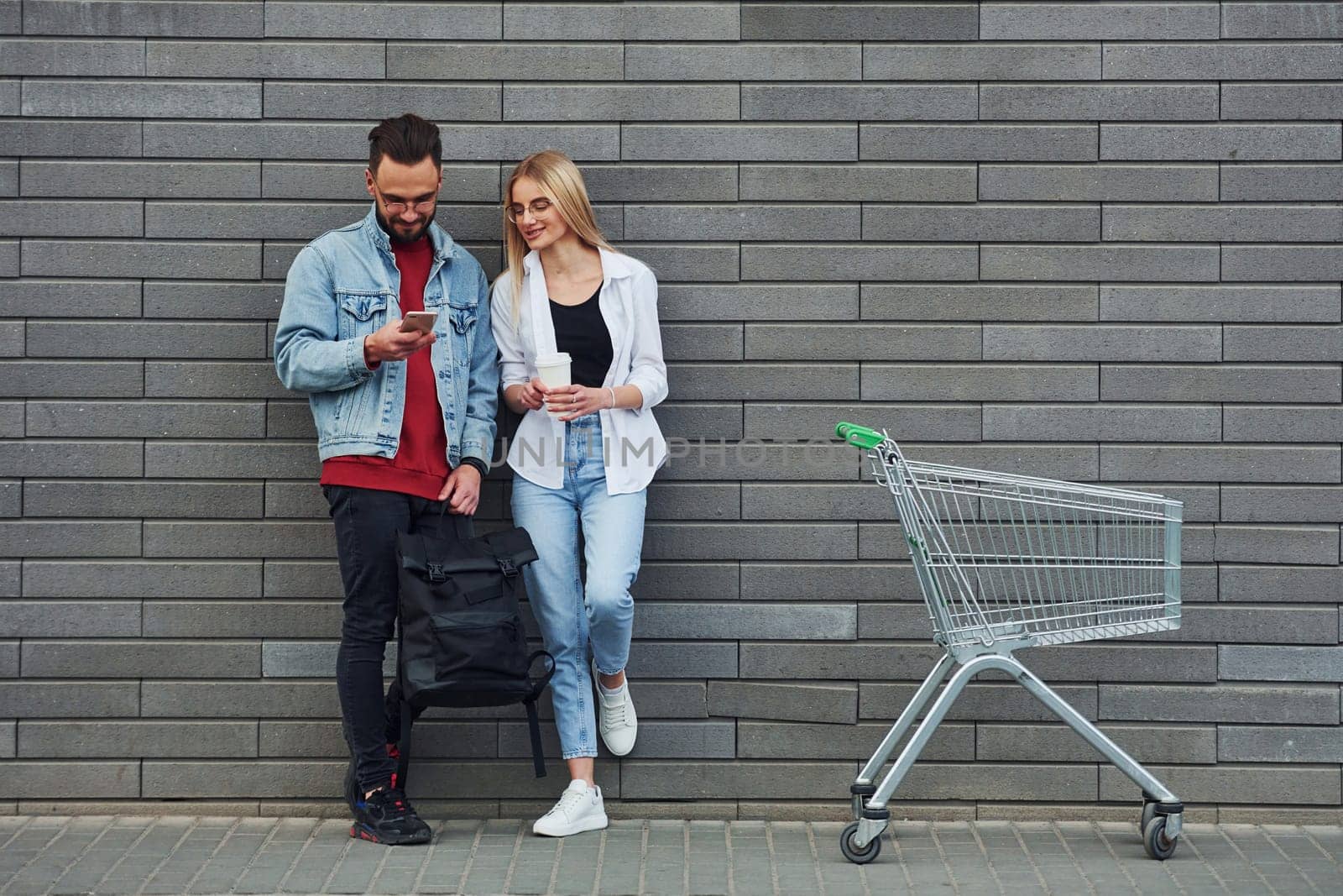 With shopping cart. Young stylish man with woman in casual clothes outdoors together. Conception of friendship or relationships.