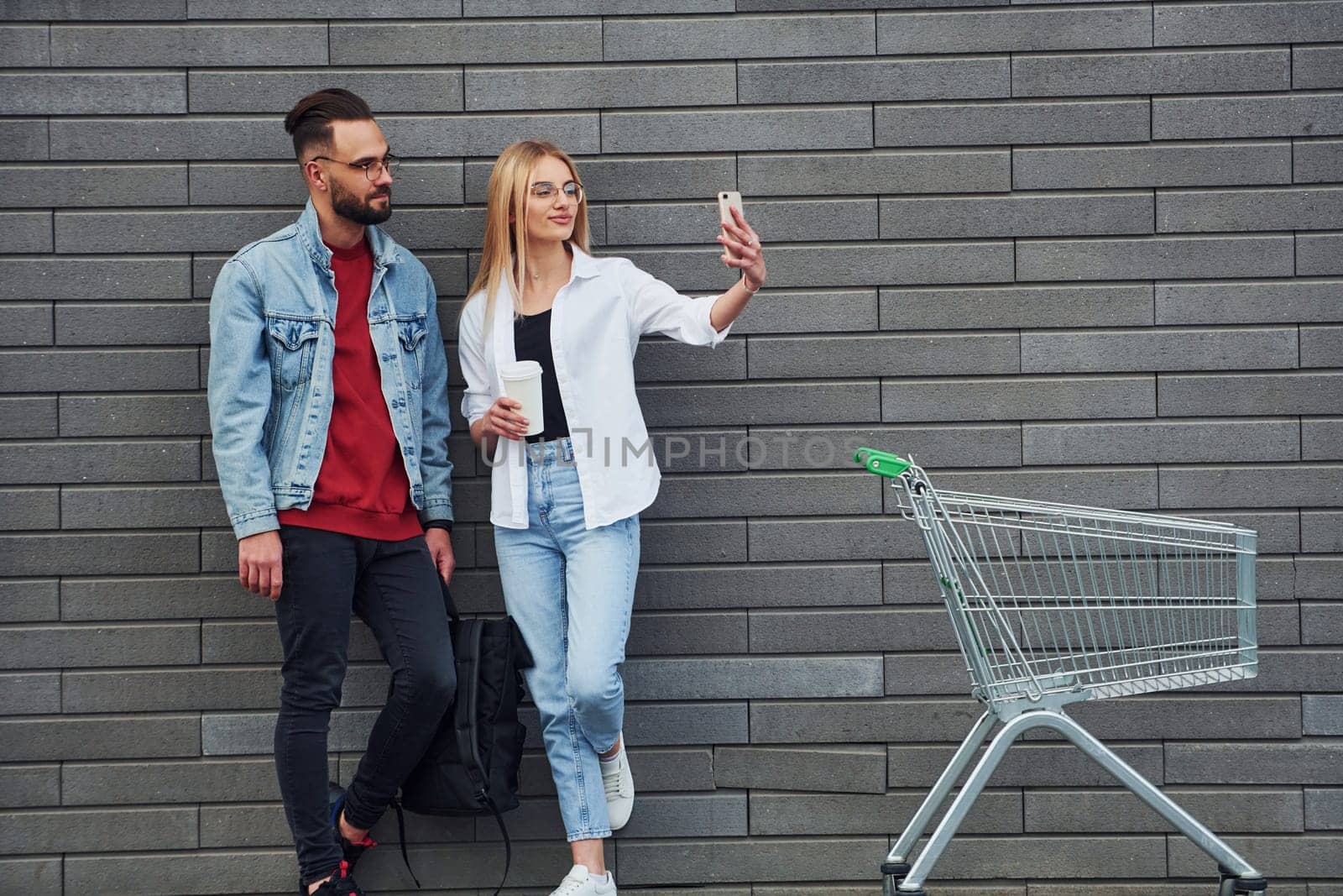 With shopping cart. Young stylish man with woman in casual clothes outdoors together. Conception of friendship or relationships.