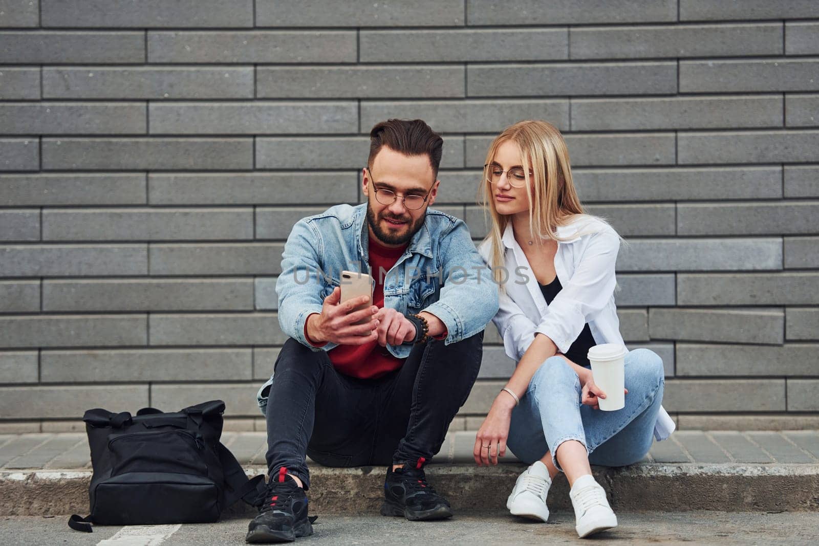 Young stylish man with woman in casual clothes sitting outdoors together. Conception of friendship or relationships.