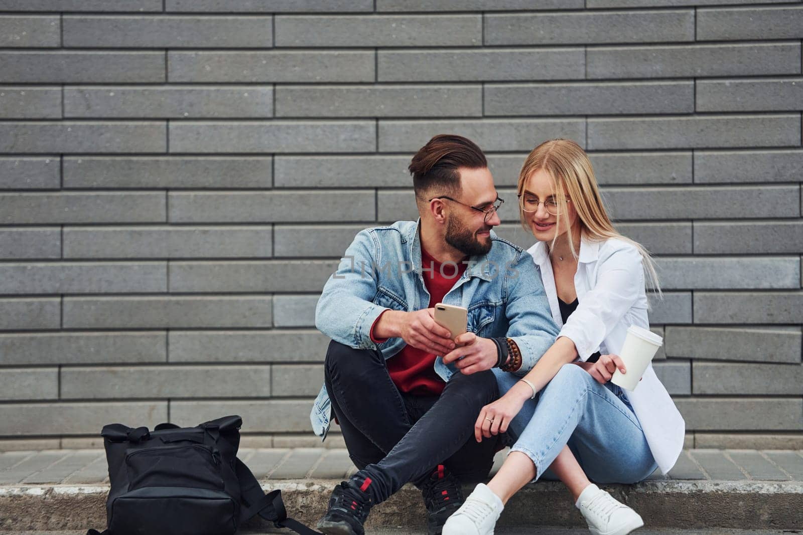 Young stylish man with woman in casual clothes sitting outdoors together. Conception of friendship or relationships.