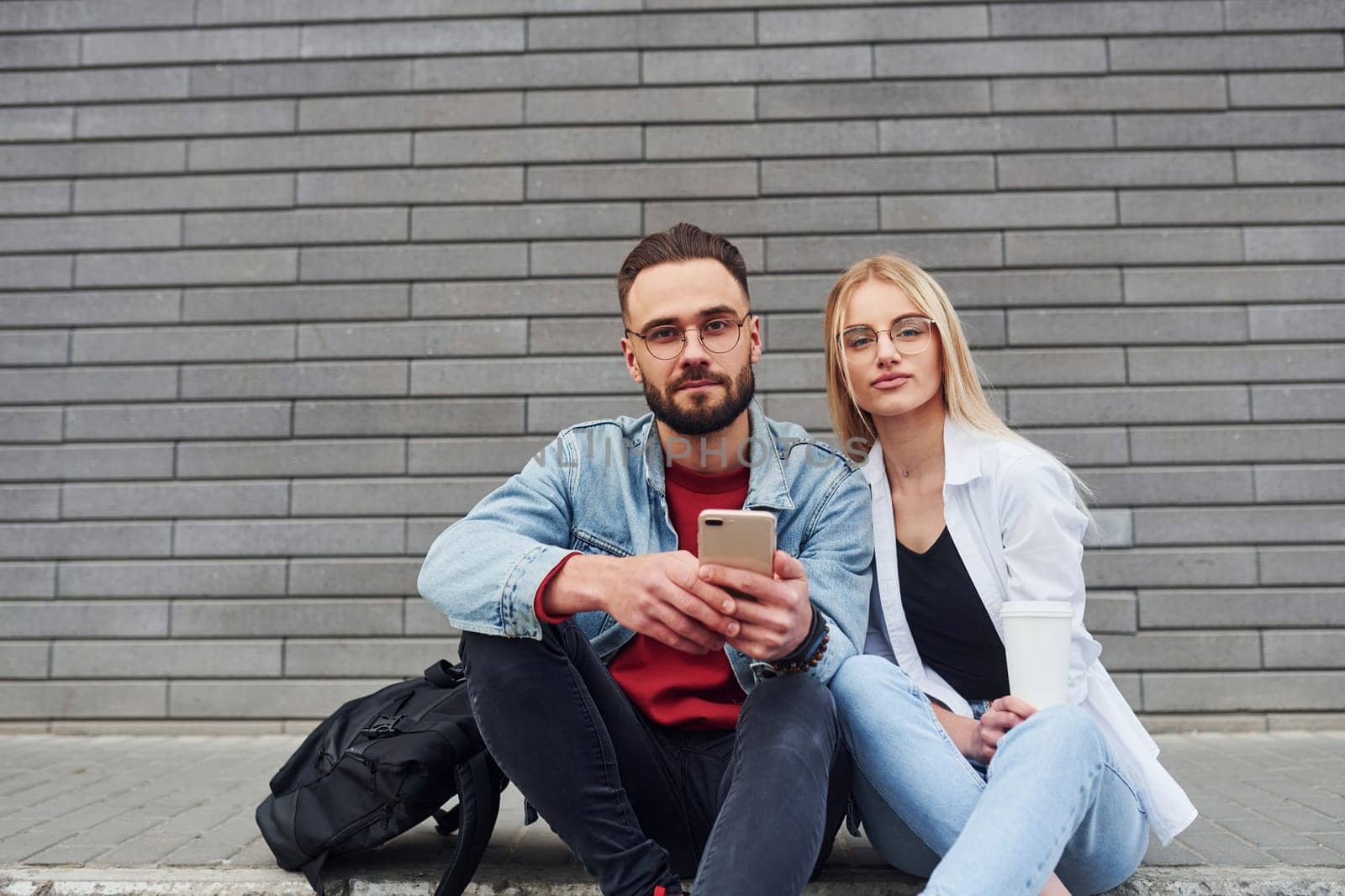 Using phone. Young stylish man with woman in casual clothes sitting outdoors together. Conception of friendship or relationships.