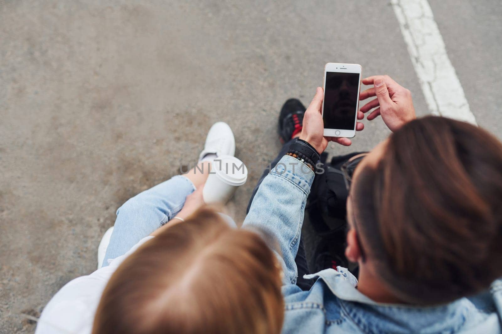 Using phone. Young stylish man with woman in casual clothes sitting outdoors together. Conception of friendship or relationships.