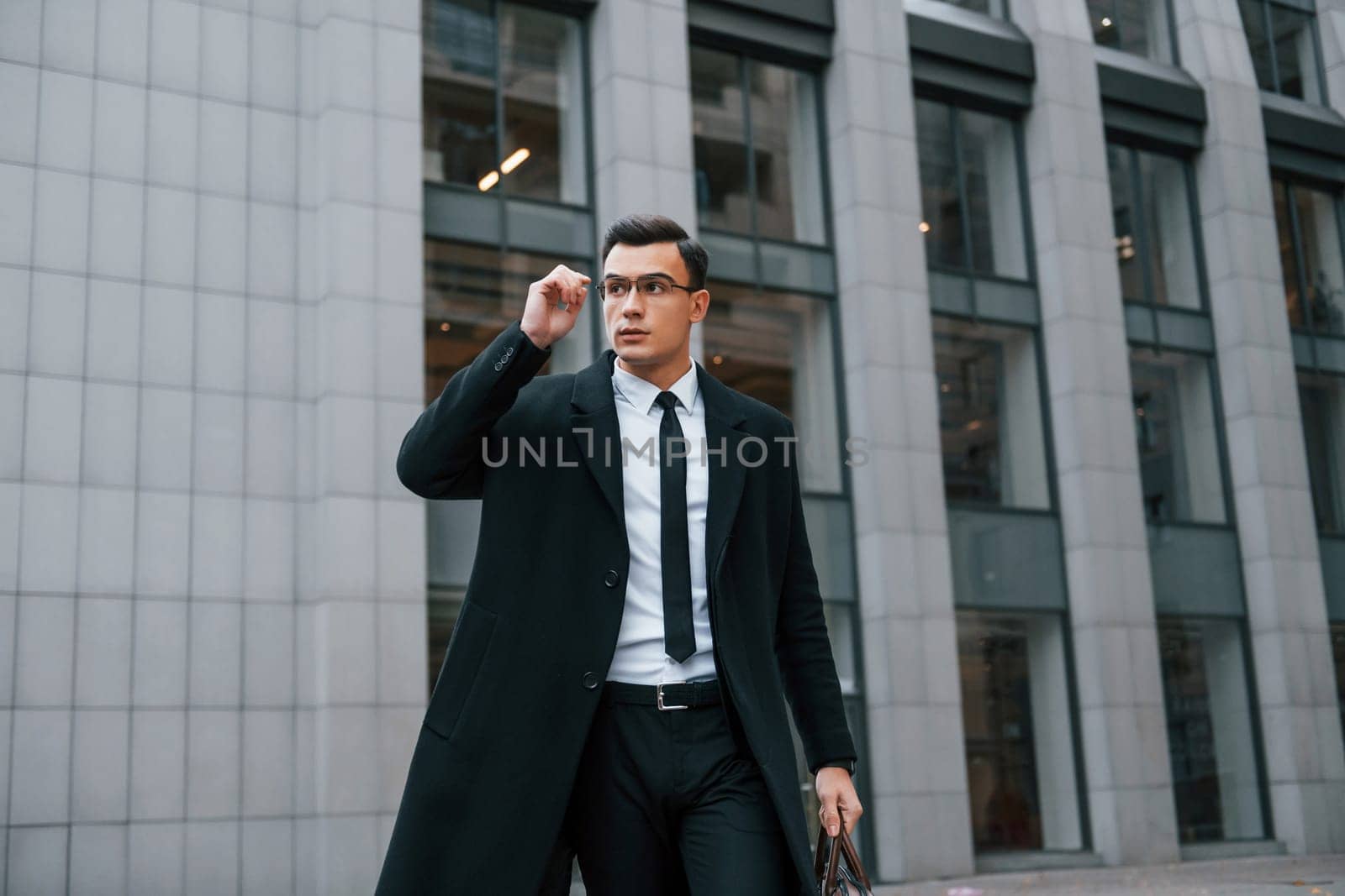 Conception of formal clothes. Businessman in black suit and tie is outdoors in the city by Standret