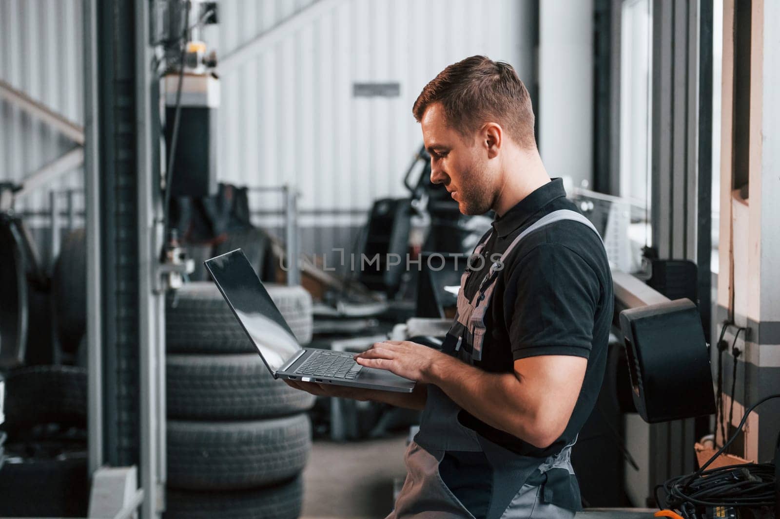 Holding laptop in hands. Man in uniform is working in the auto service.