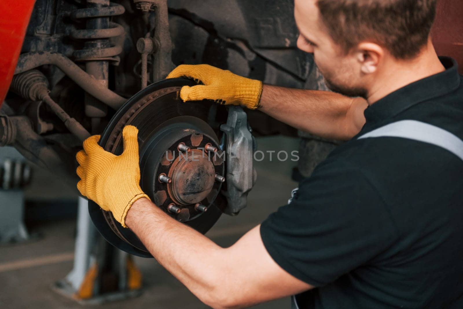 Fixing breaks. Man in uniform is working in the auto service.