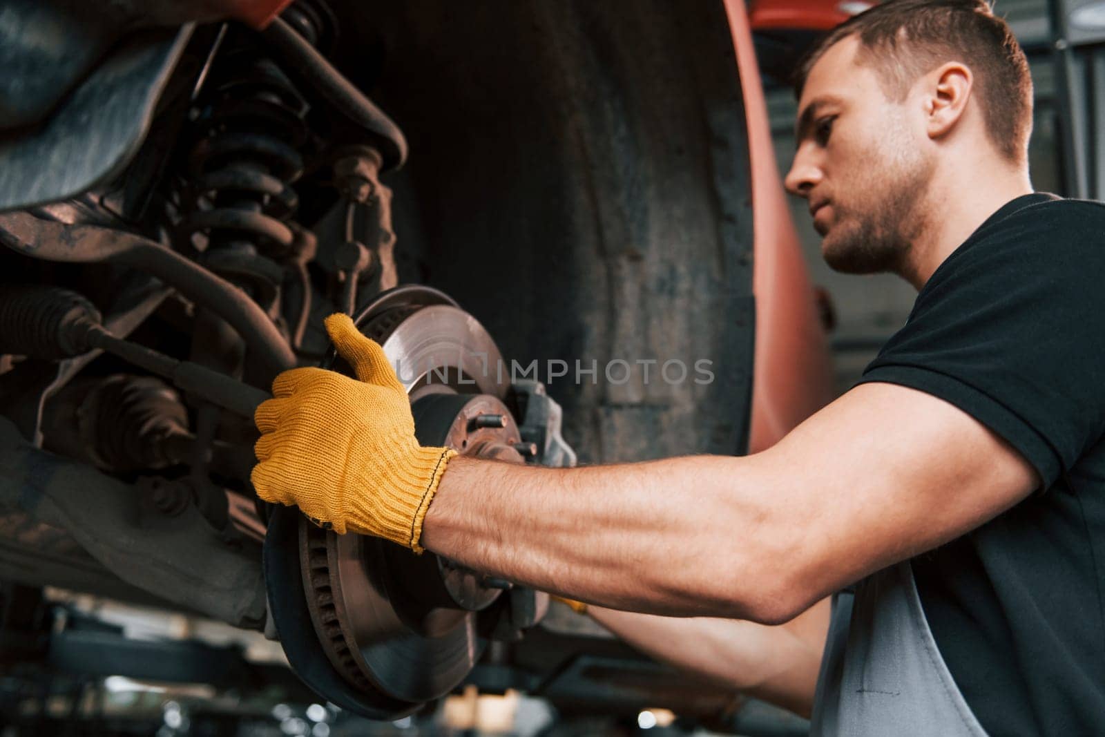 Fixing breaks. Man in uniform is working in the auto service.