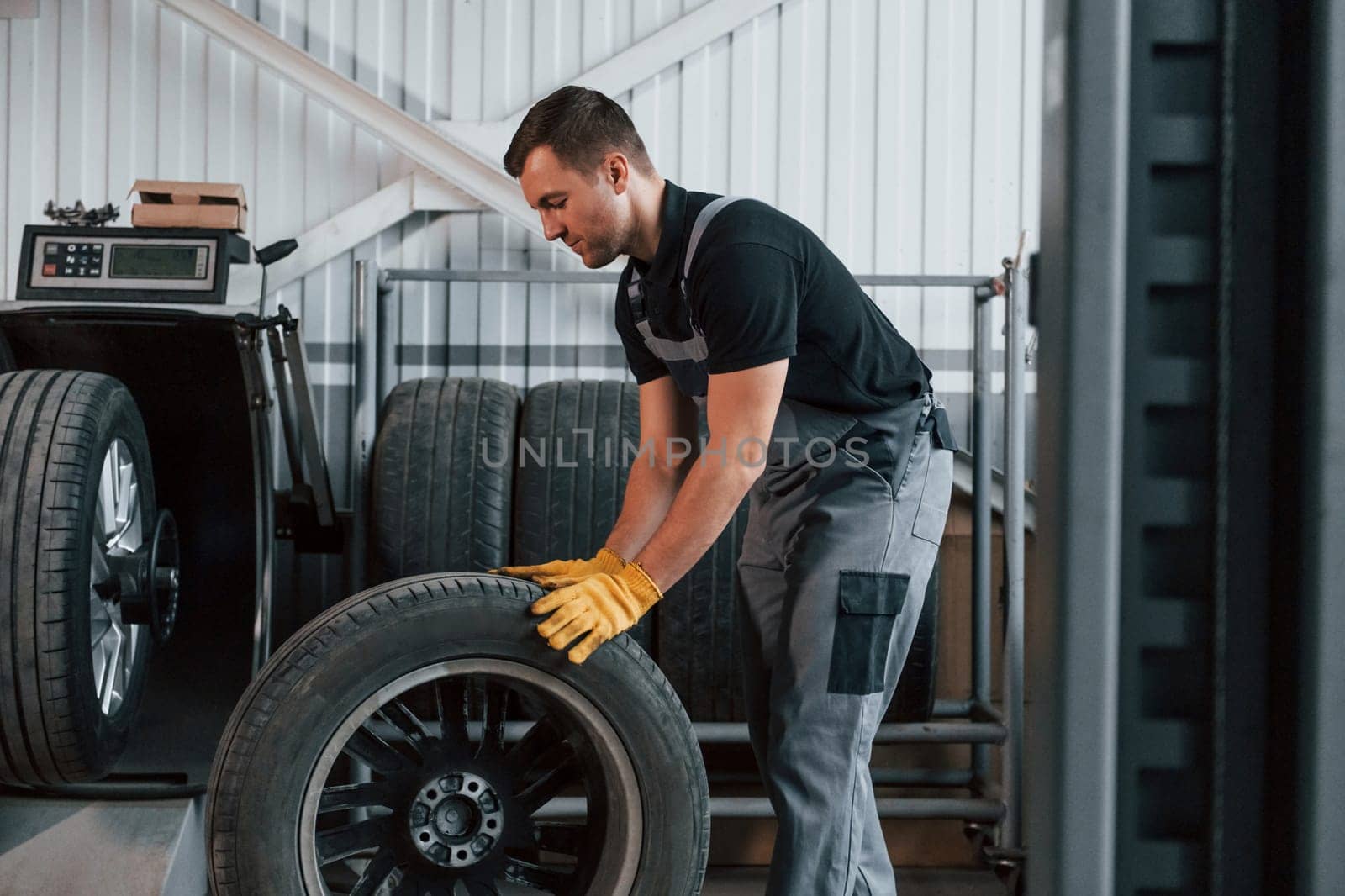 Working with broken wheel. Man in uniform is working in the auto service.