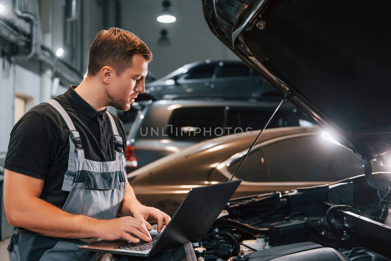Side view. Man in uniform is working in the auto service.