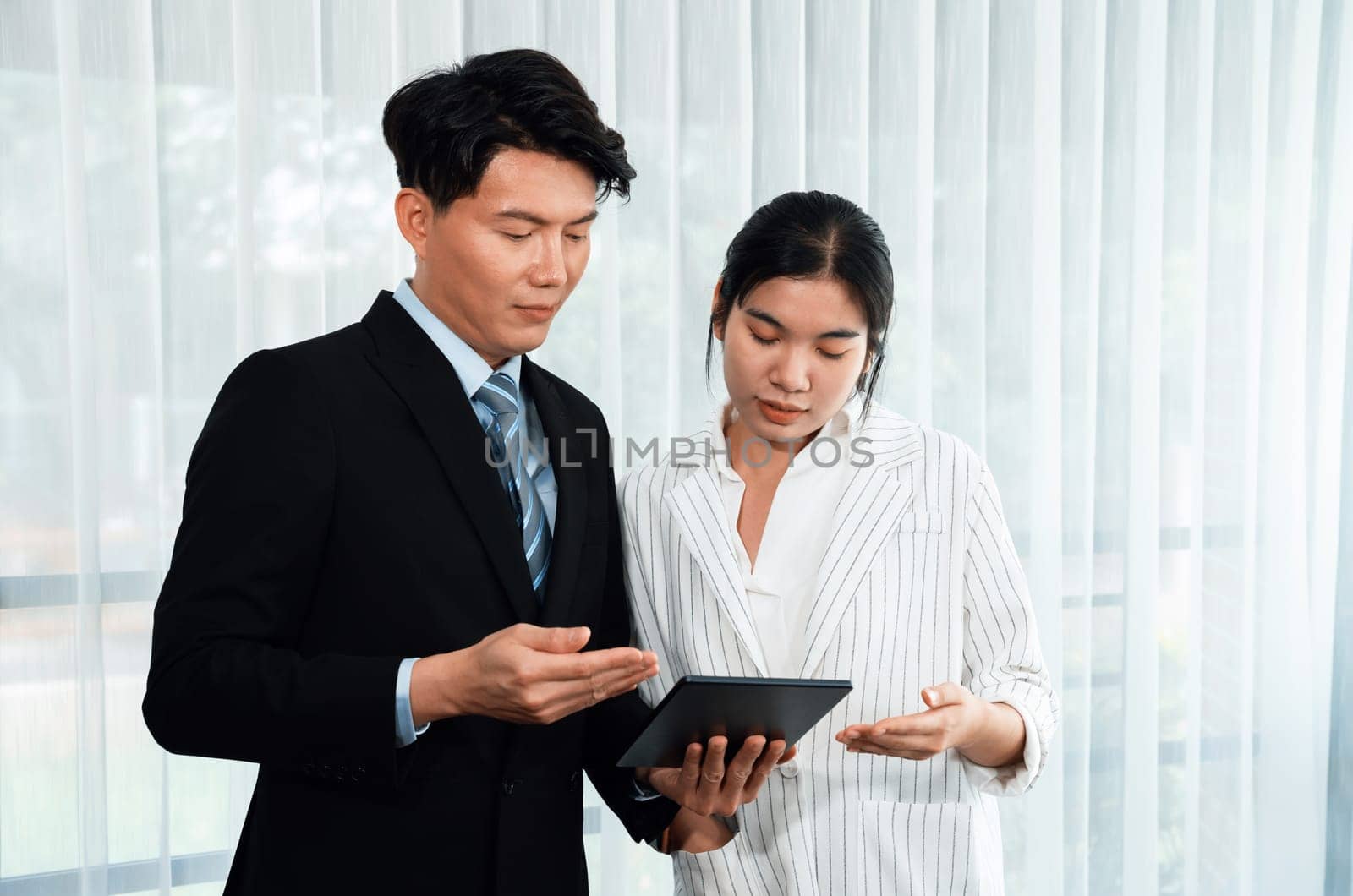 Manager advising guiding younger colleague with tablet in workplace. Couple businesspeople in formal wear working together on financial strategy as concept of teamwork and harmony in office.