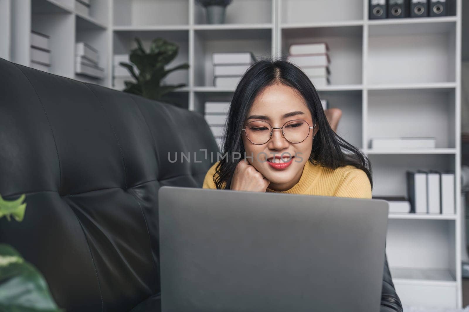 Young woman enjoys success looking at the laptop screen while lay on a cozy sofa in the living room of the house...