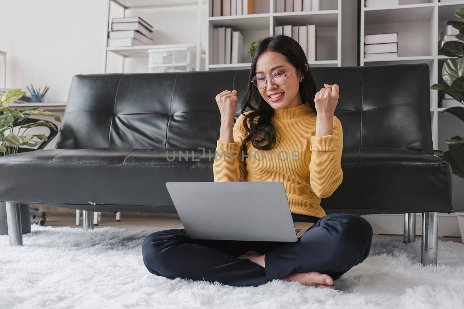 Happy young Asian business woman successful excited raised hand rejoicing with laptop at home...