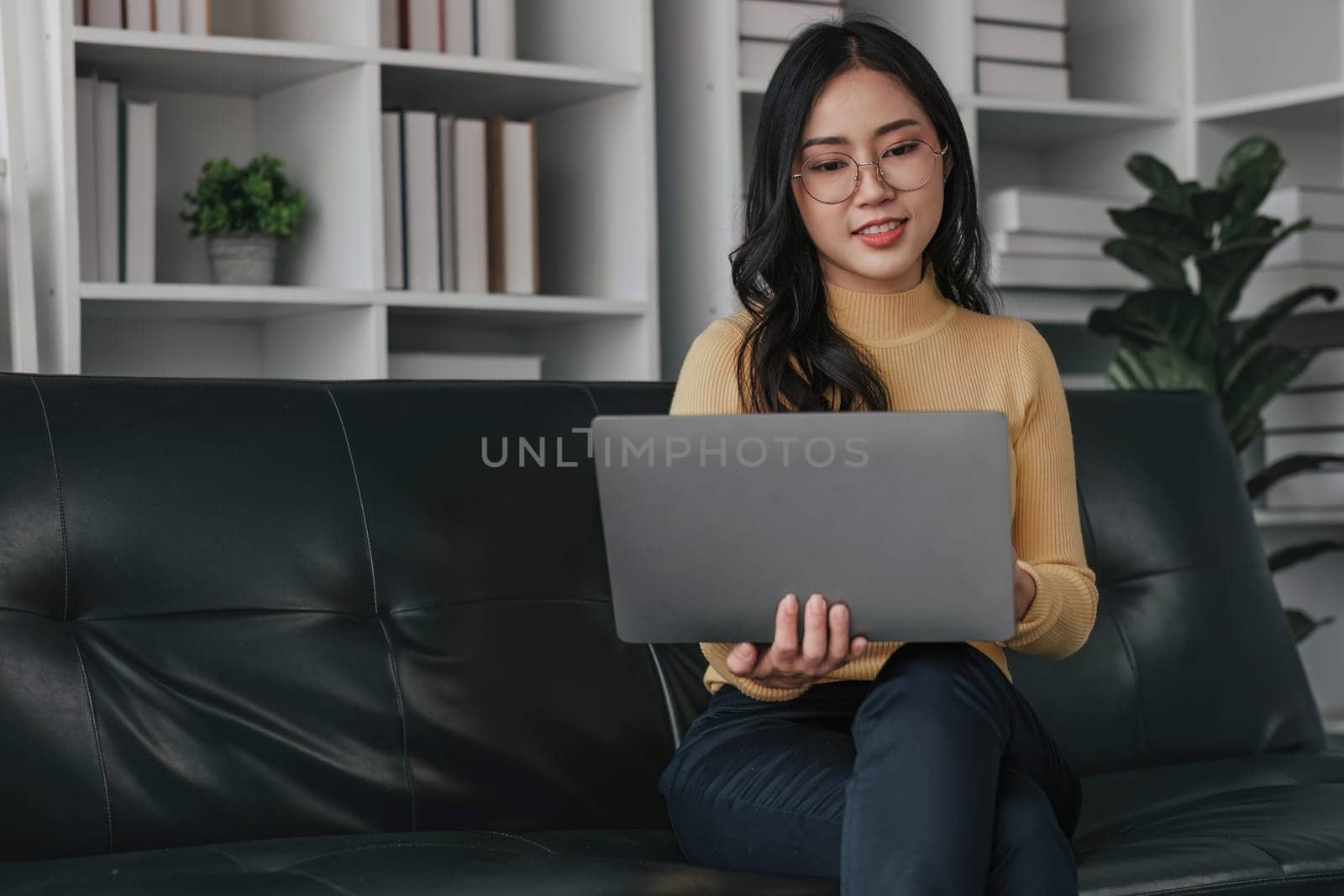 Young asian woman in good spirits working on laptop at home while sitting on the couch..
