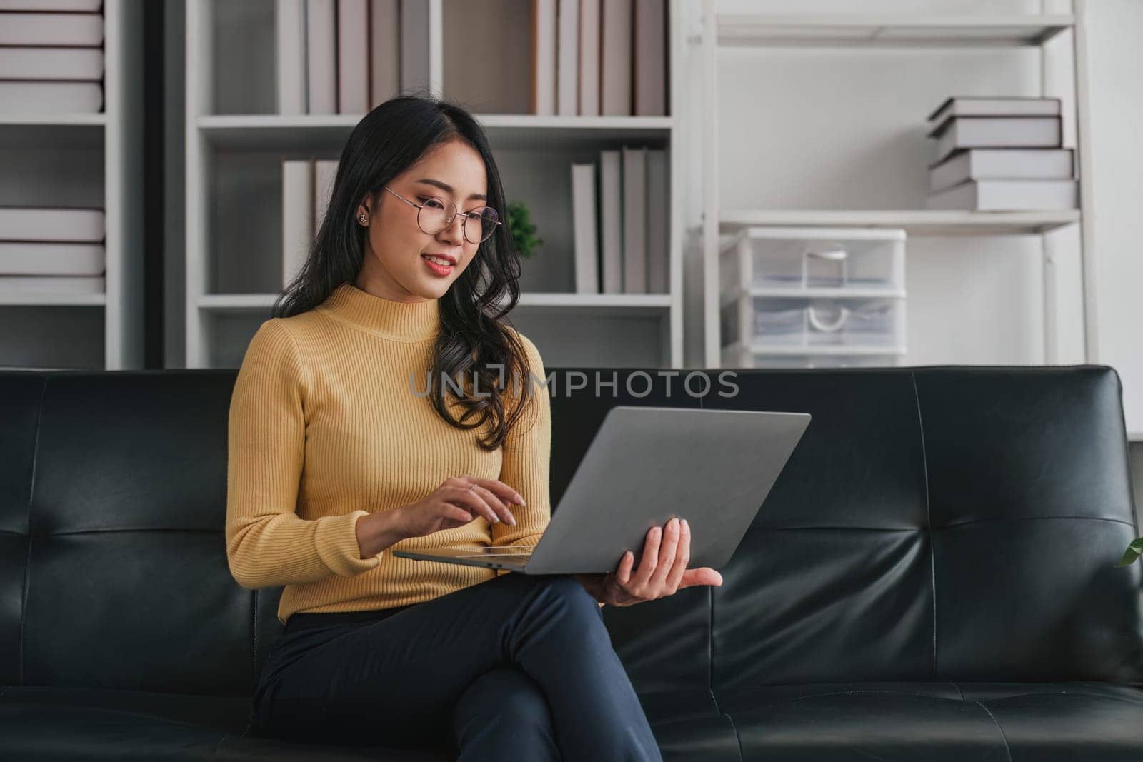 Young asian woman in good spirits working on laptop at home while sitting on the couch..