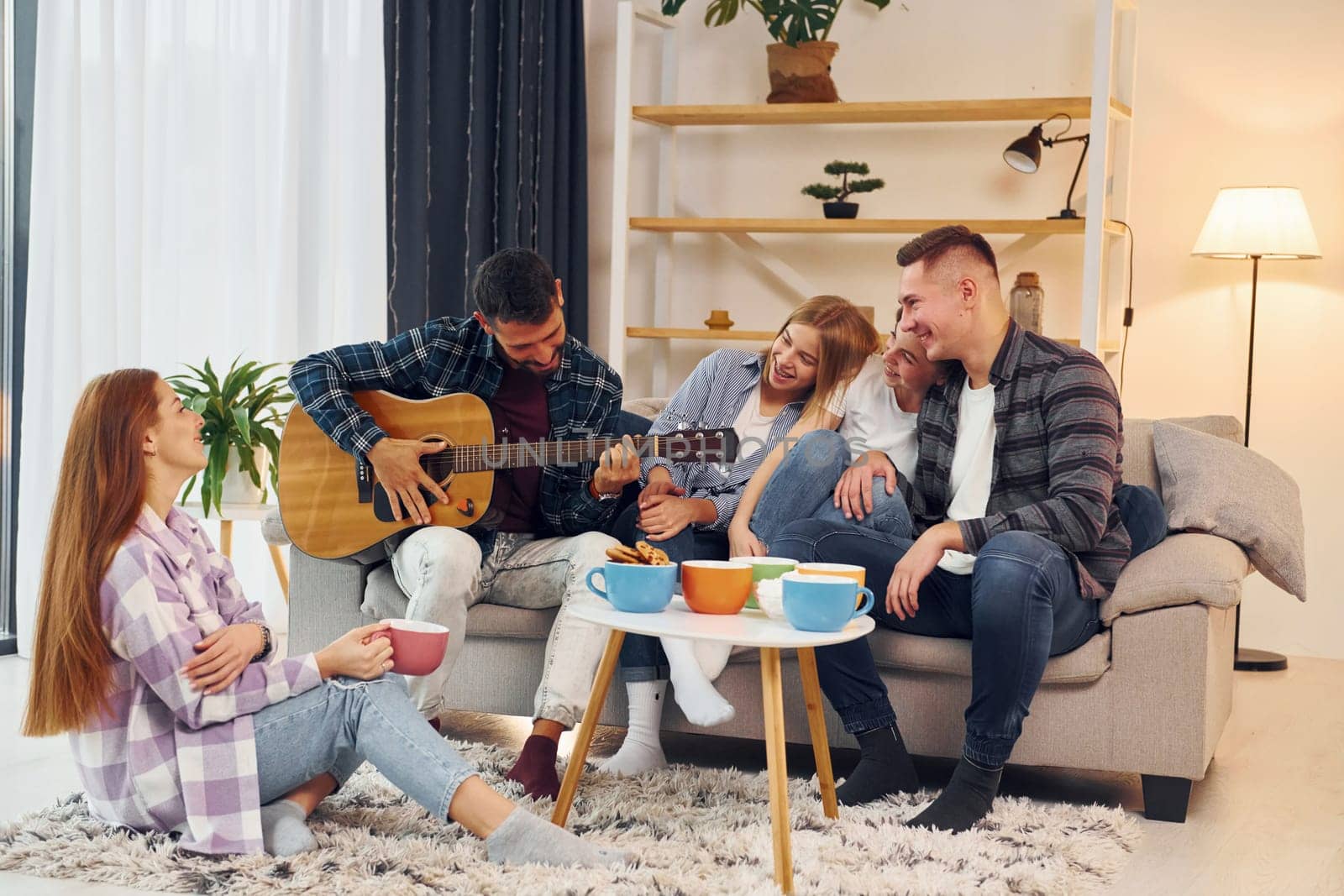 Playing acoustic guitar. Group of friends have party indoors together.