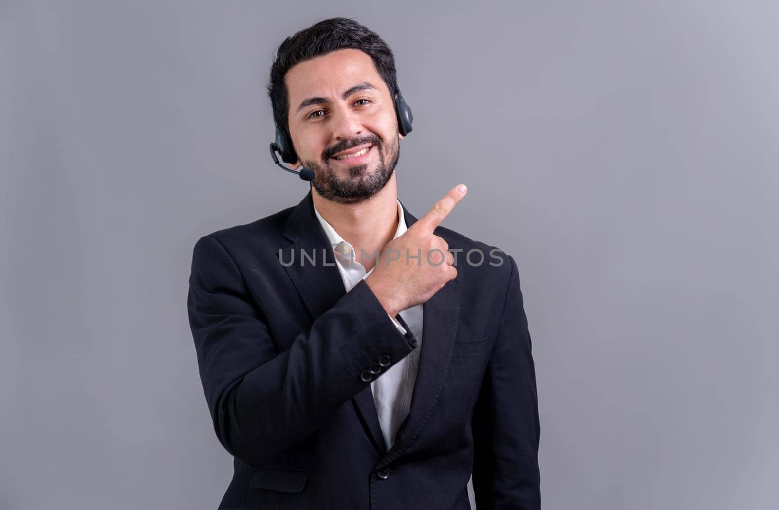 Male call center operator wearing headset and formal suit finger pointing at customizable empty space on isolated background portrait. Professional smile for customer service and support. fervent