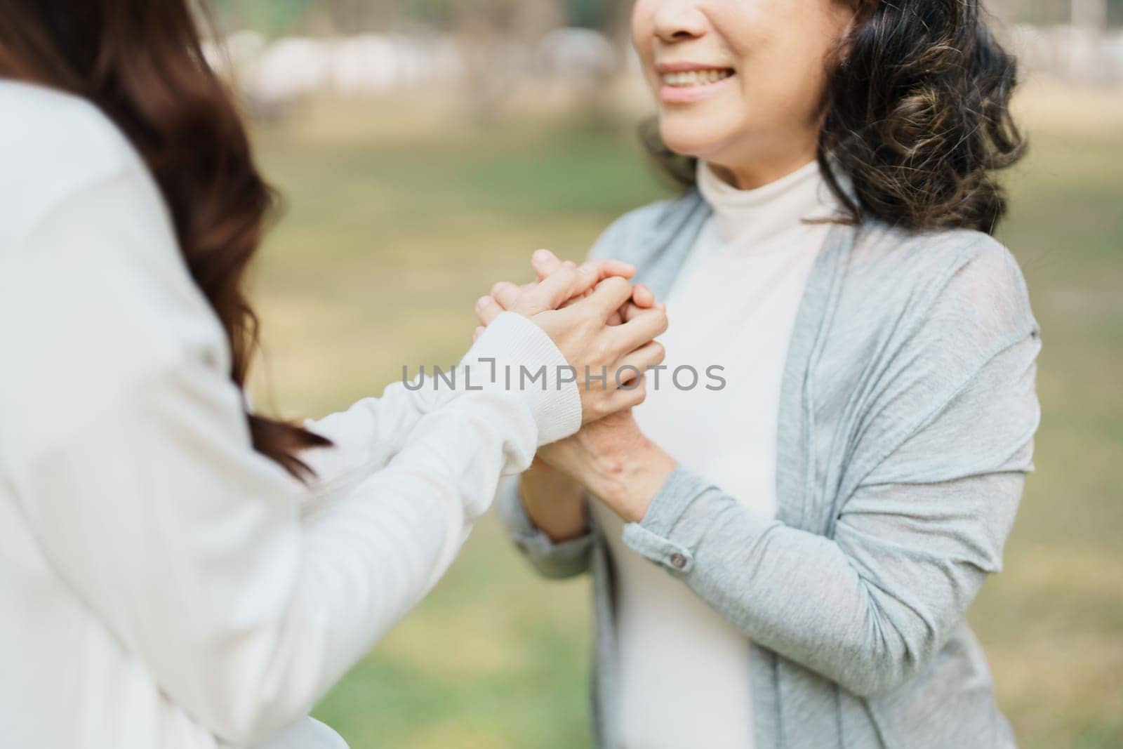 Adult daughter holding her elderly mother hand with love and walk together in park by Manastrong