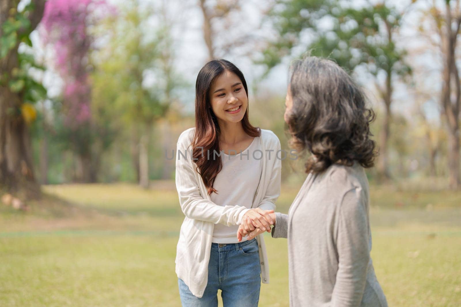 Adult daughter holding her elderly mother hand with love and walk together in park.