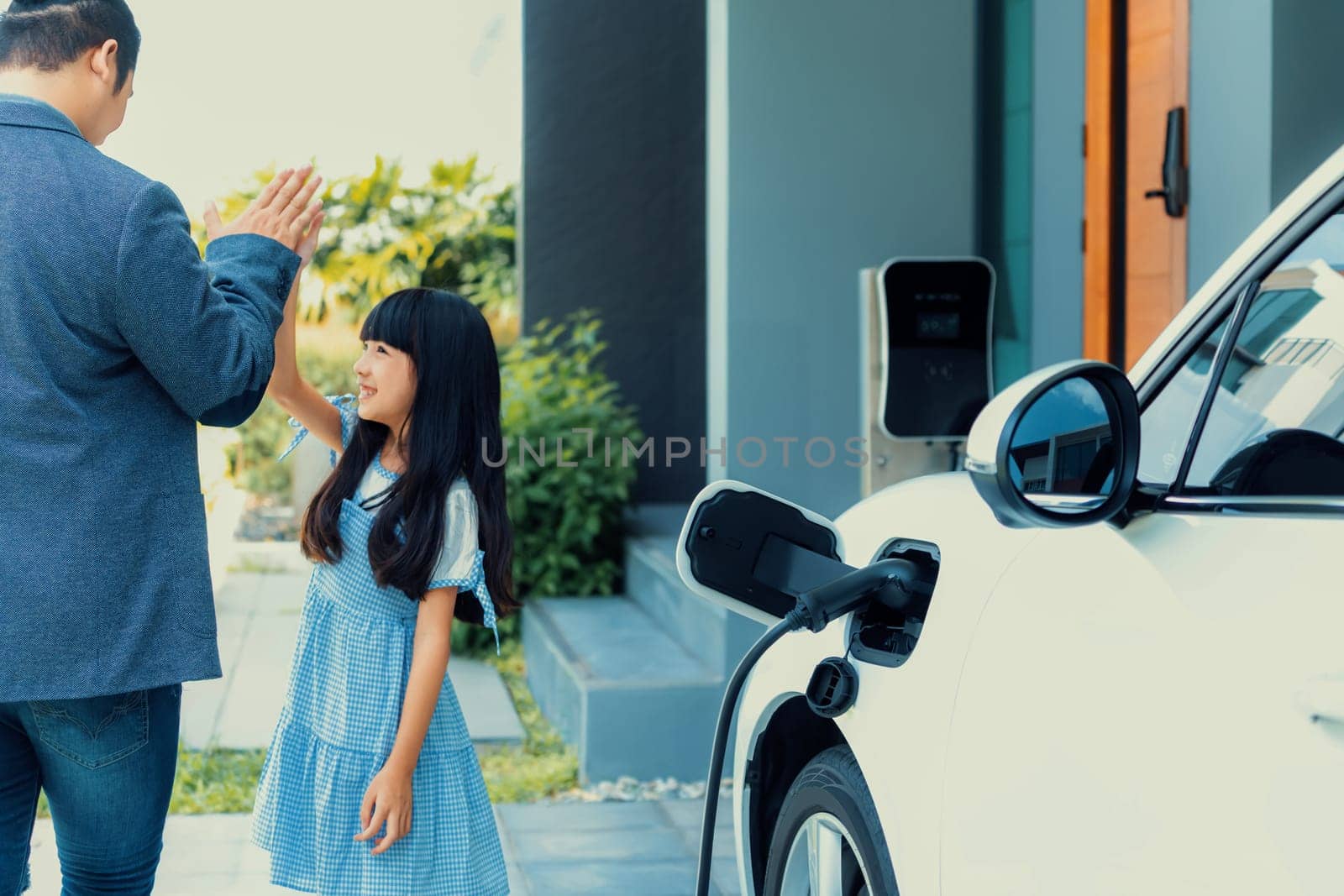 Progressive father and daughter returned from school in electric vehicle that is being charged at home. Electric vehicle driven by renewable clean energy. Home charging station concept for environment