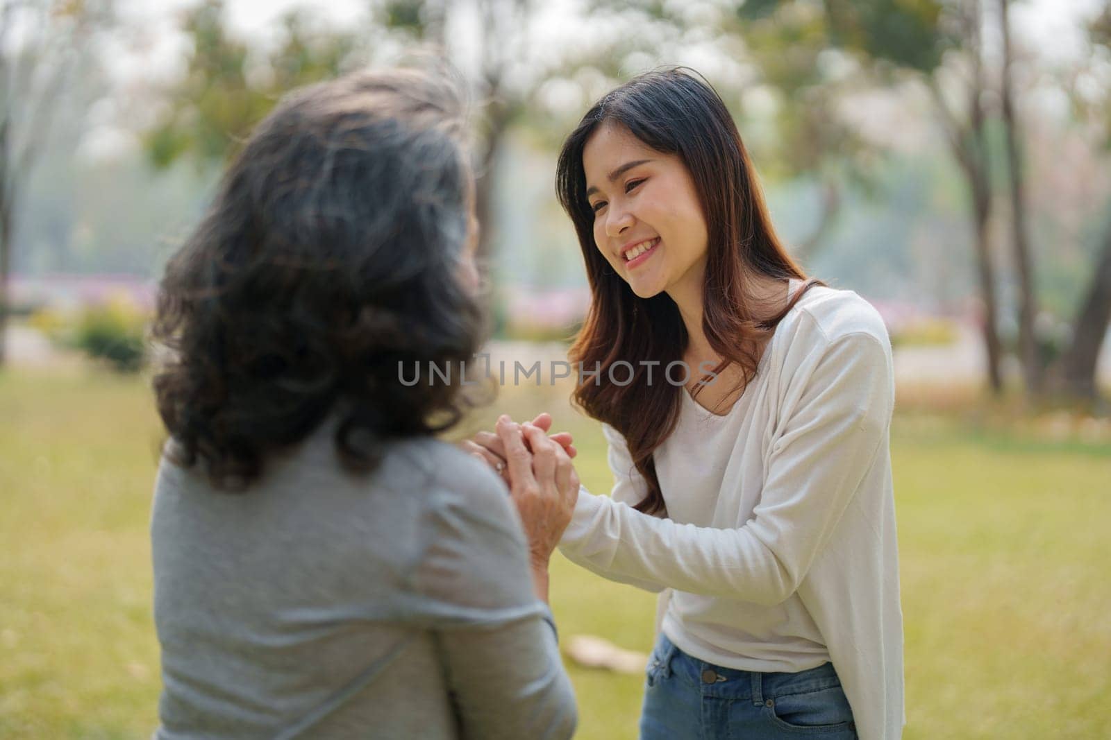 Adult daughter holding her elderly mother hand with love and walk together in park.