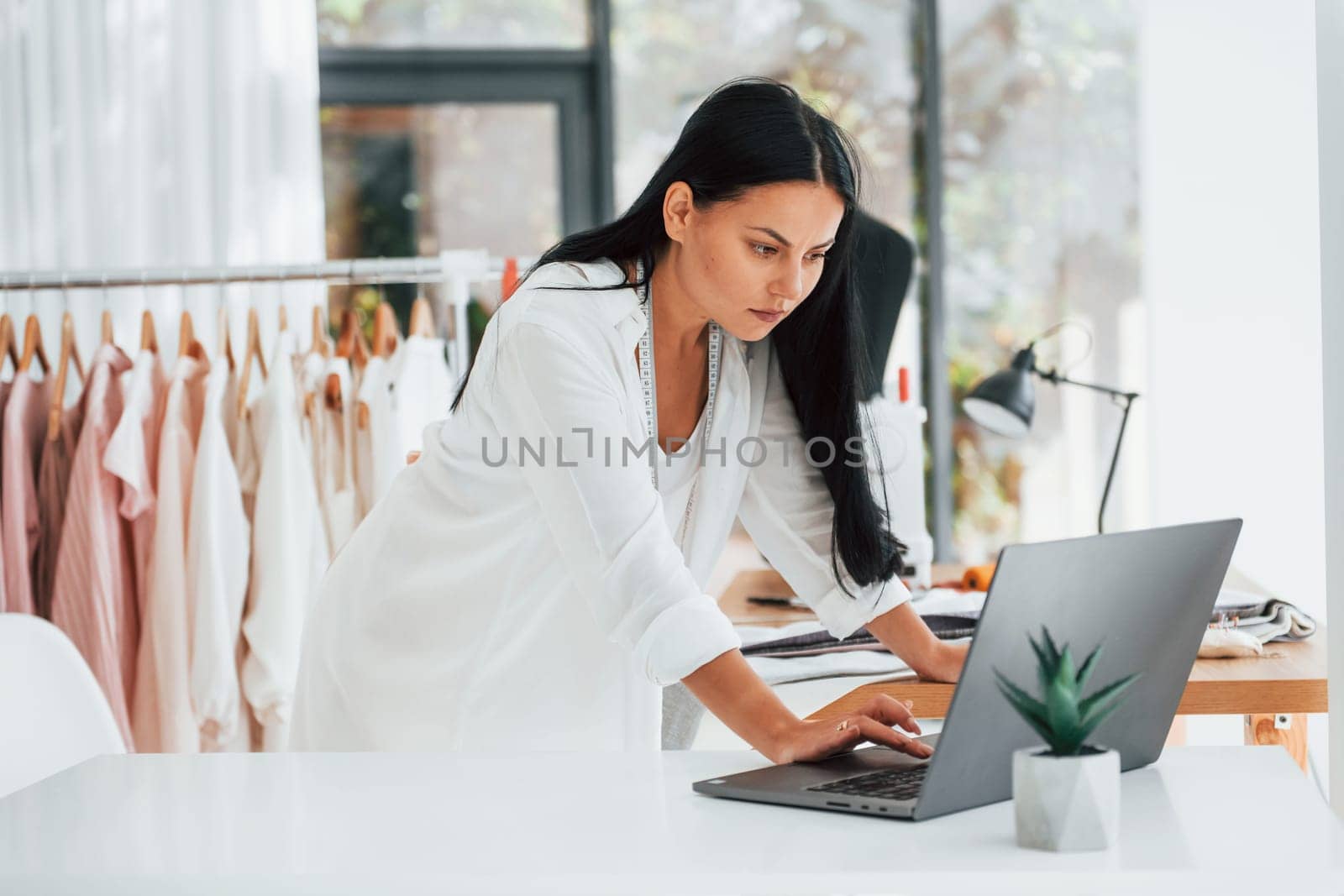 Using laptop. Seamstress is in her office that is with different clothes.