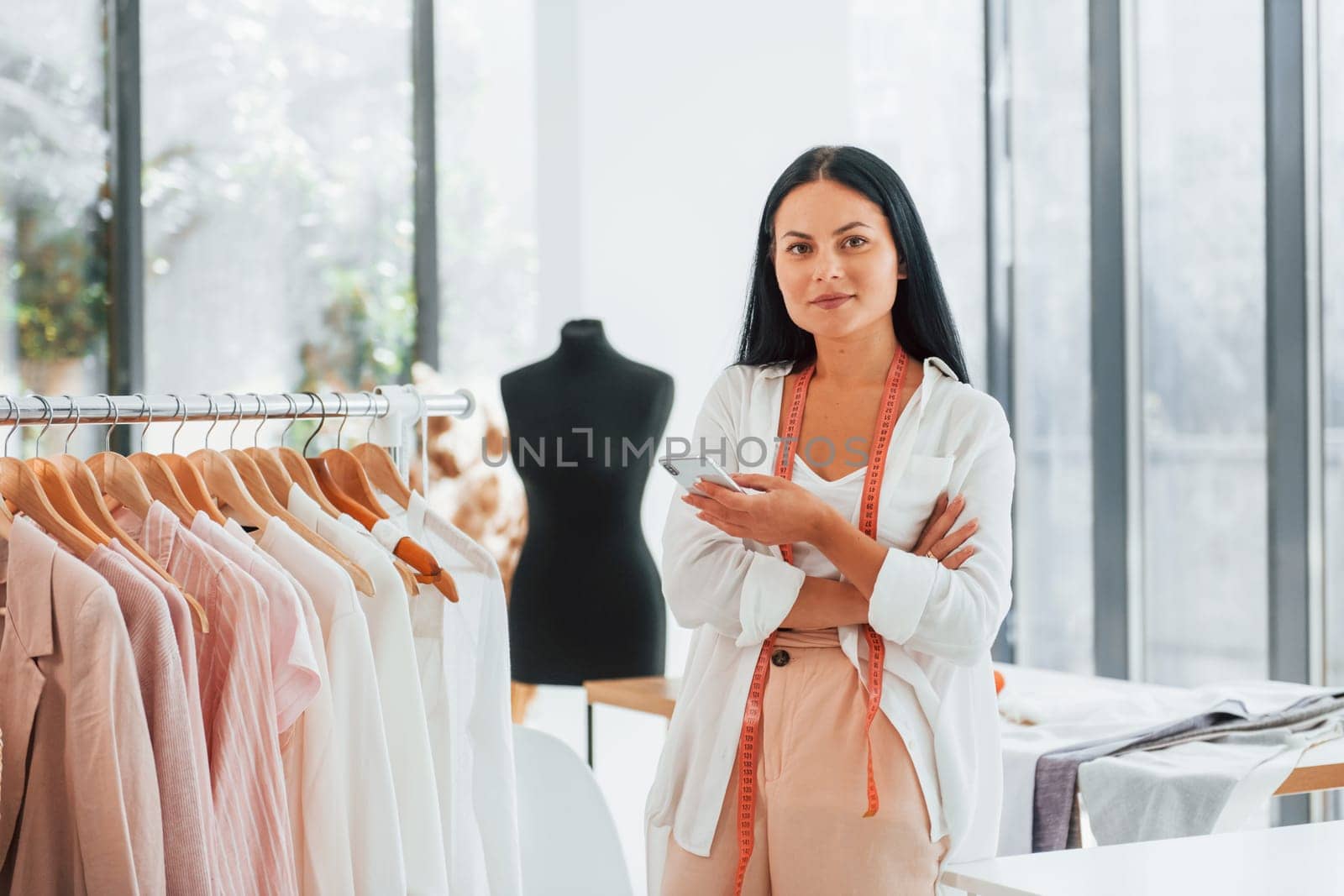Standing and smiling. Seamstress is in her office that is with different clothes.