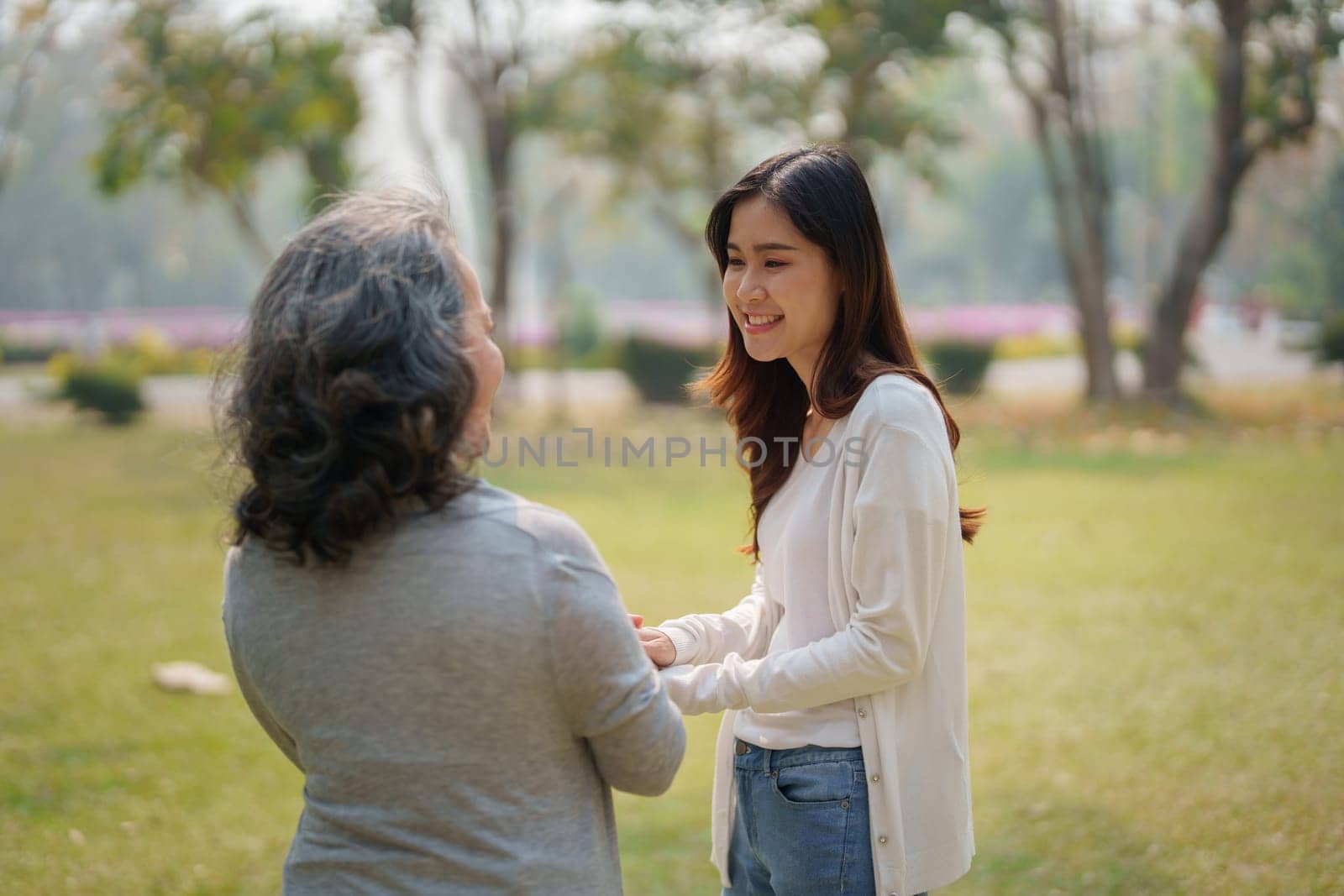 Adult daughter holding her elderly mother hand with love and walk together in park by Manastrong