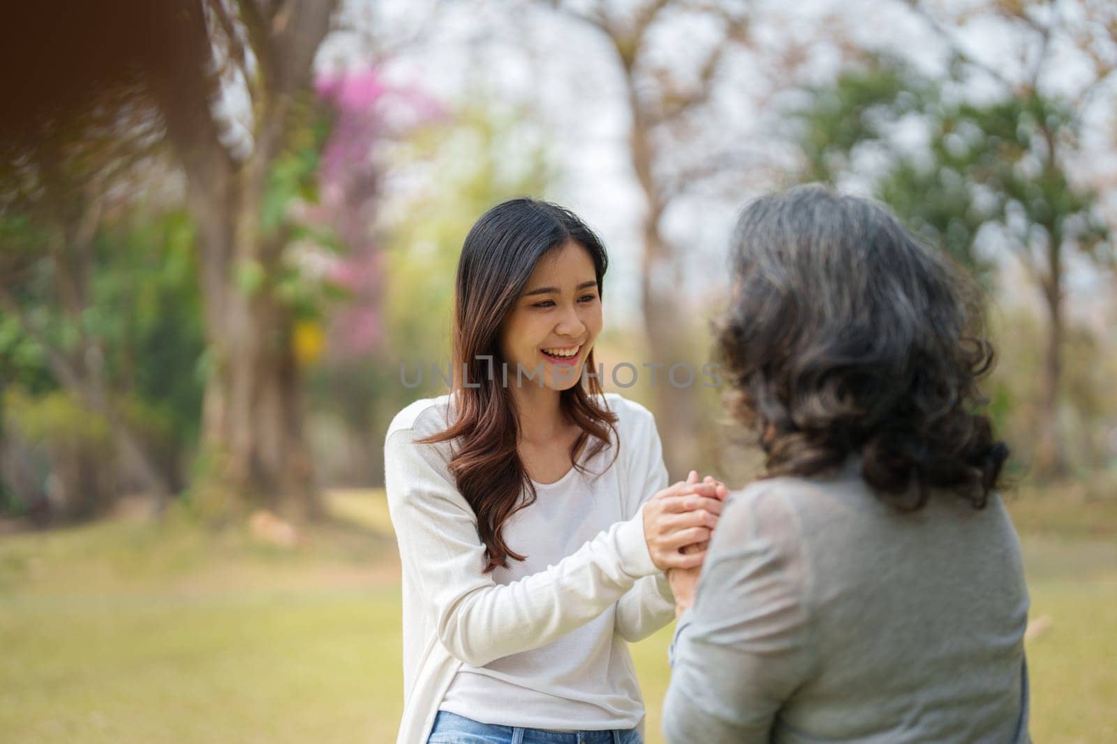 Adult daughter holding her elderly mother hand with love and walk together in park.